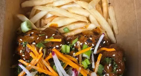 Chicken wings topped with shredded carrots, green onions, sesame seeds, and sliced red onions, served with French fries.