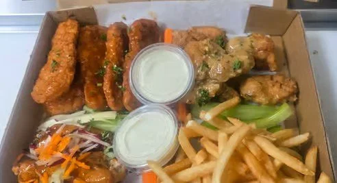 Box containing fried chicken drumsticks, chicken wings, French fries, coleslaw, and two cups of dipping sauce.