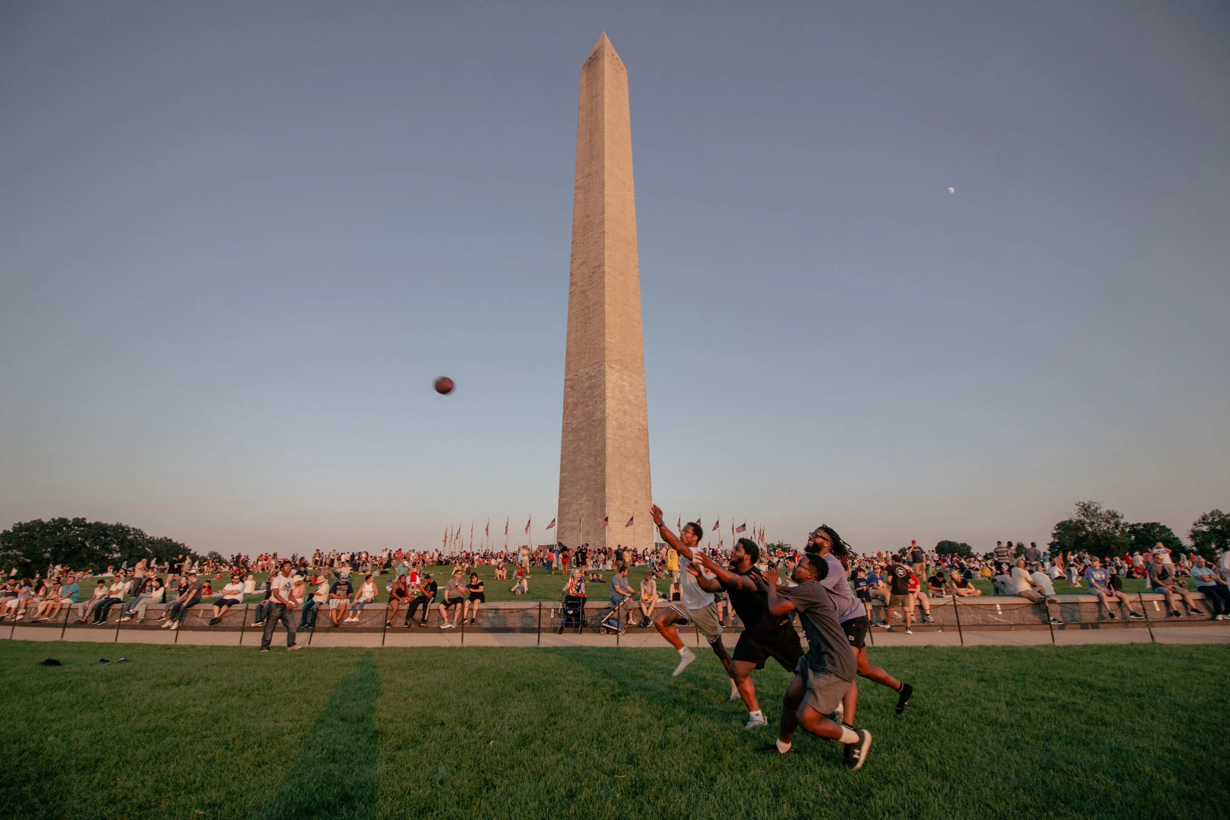 People playing volleyball at the National Mall in Washington, D.C., with the Washington Monument in the background during sunset.