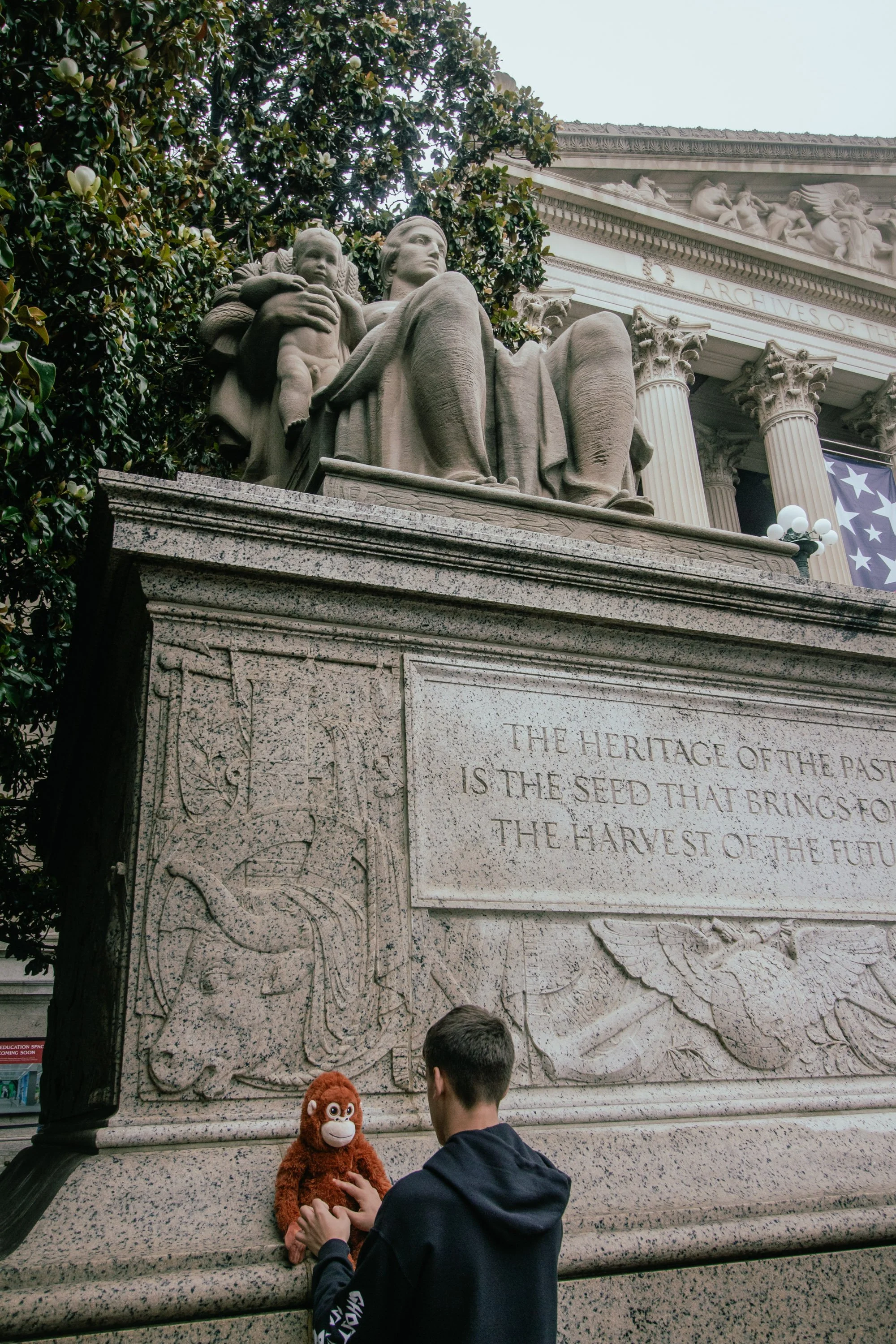 People playing with a plush orangutan toy in front of the Martin Luther King Jr. Memorial in Washington D.C., featuring classical statues and a carved stone wall with inscriptions.