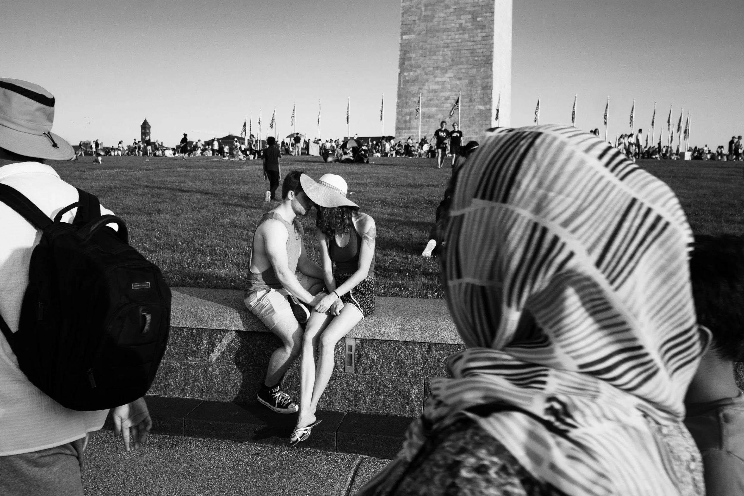 People sitting and walking in the National Mall, Washington D.C., with the Washington Monument in the background, captured in black and white.