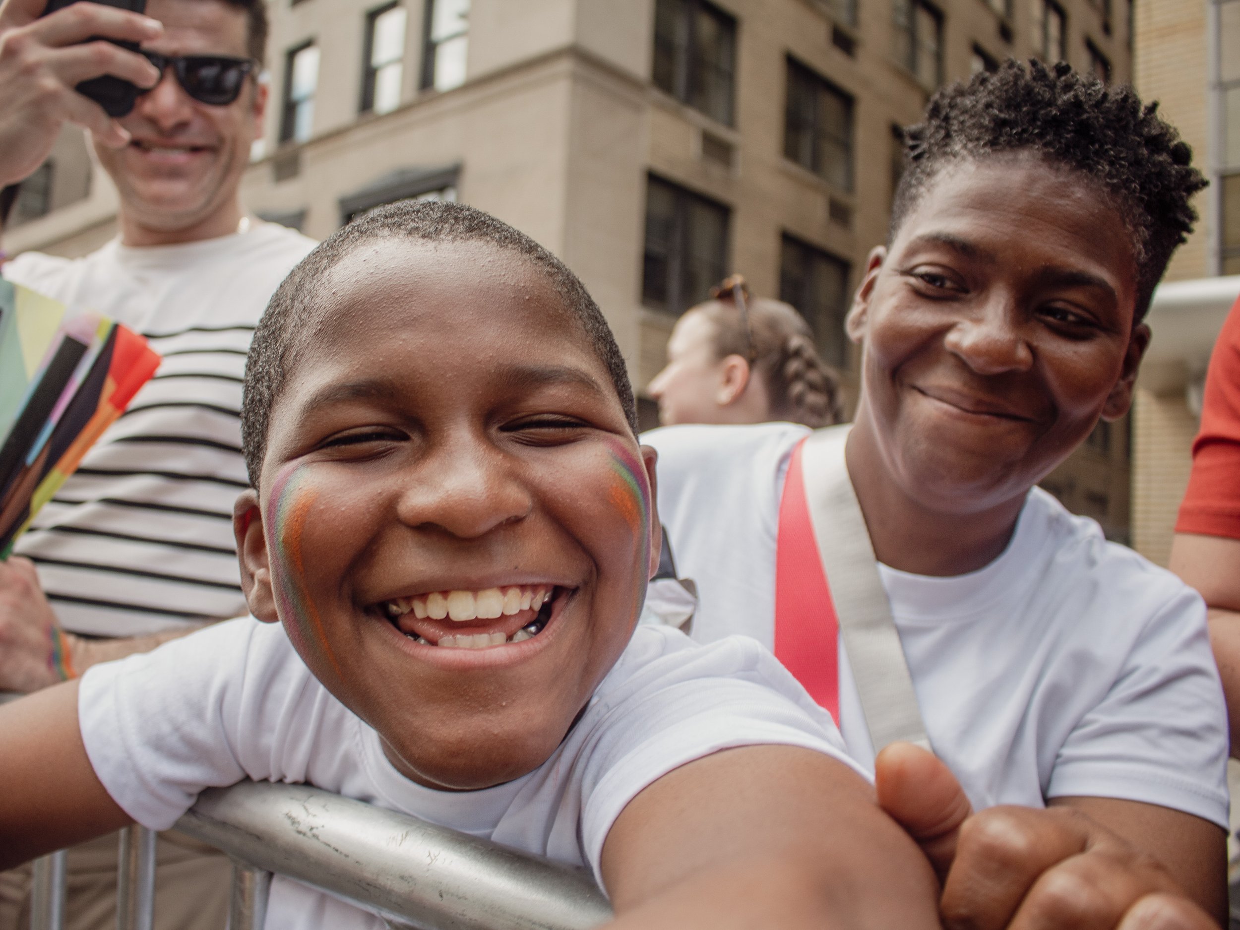 A close-up of three happy people smiling and leaning on a metal railing in an urban setting, with buildings in the background.