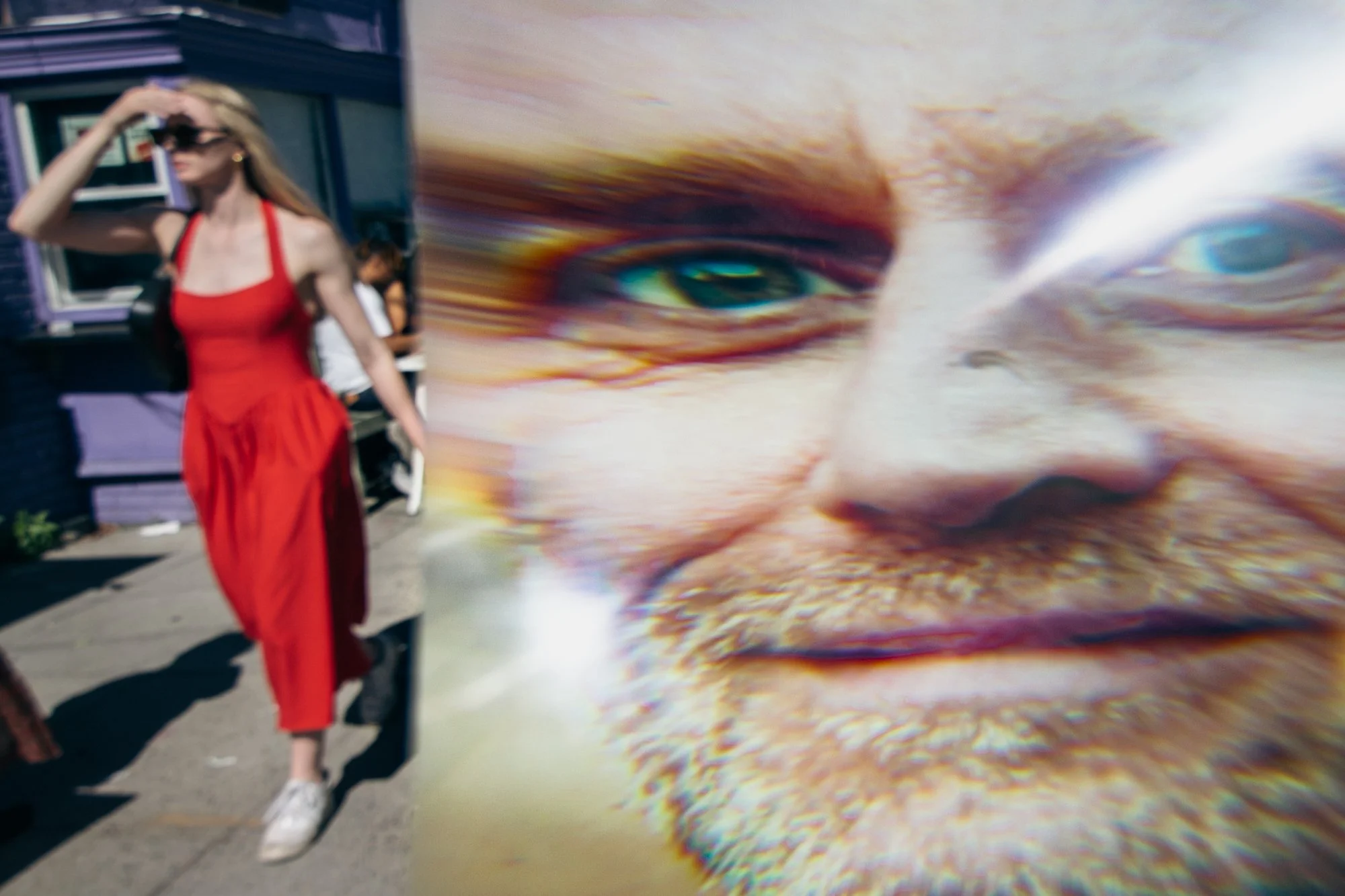 A person with long blonde hair wearing a red dress and white sneakers walking on a sidewalk, with a large colorful mural of a cat's face in the background.