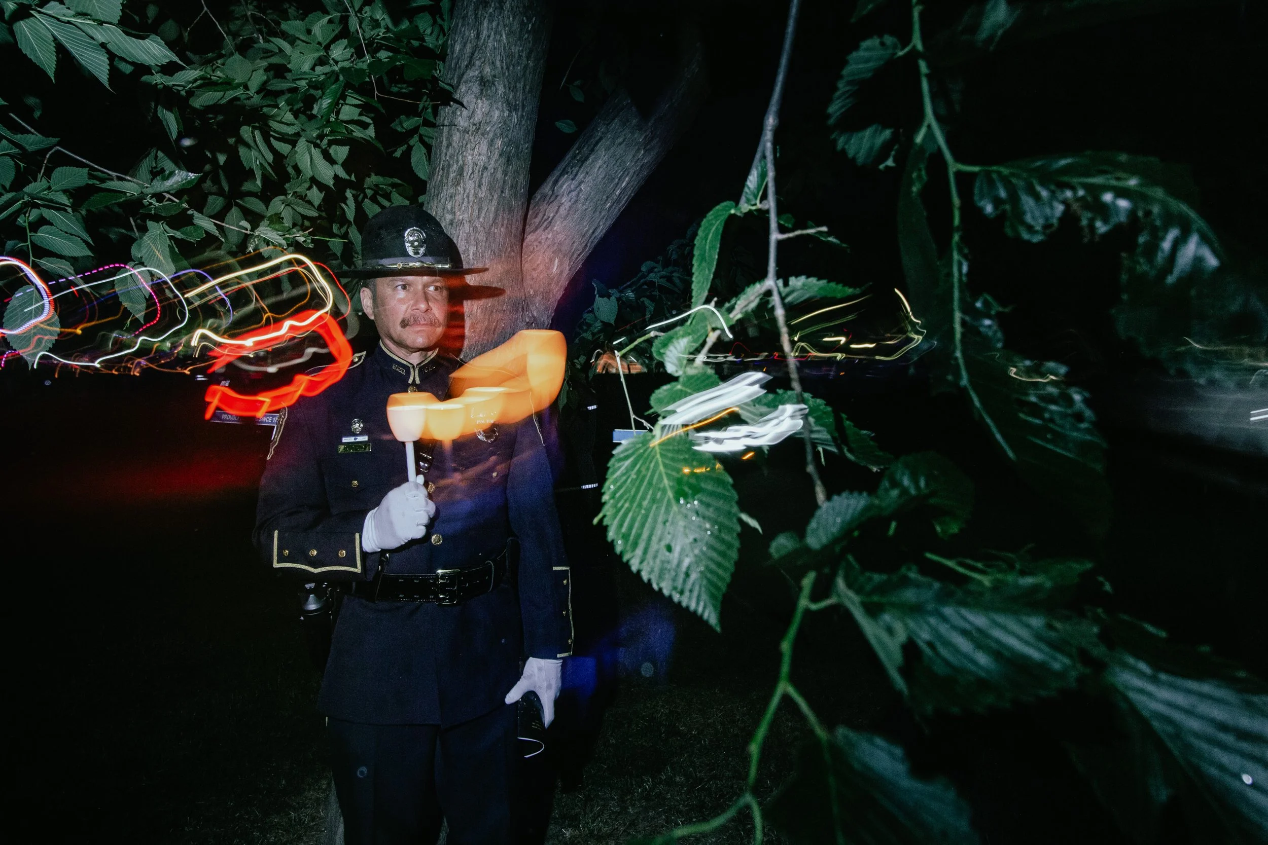 A police officer in uniform and hat holding a candle in a tree at night.