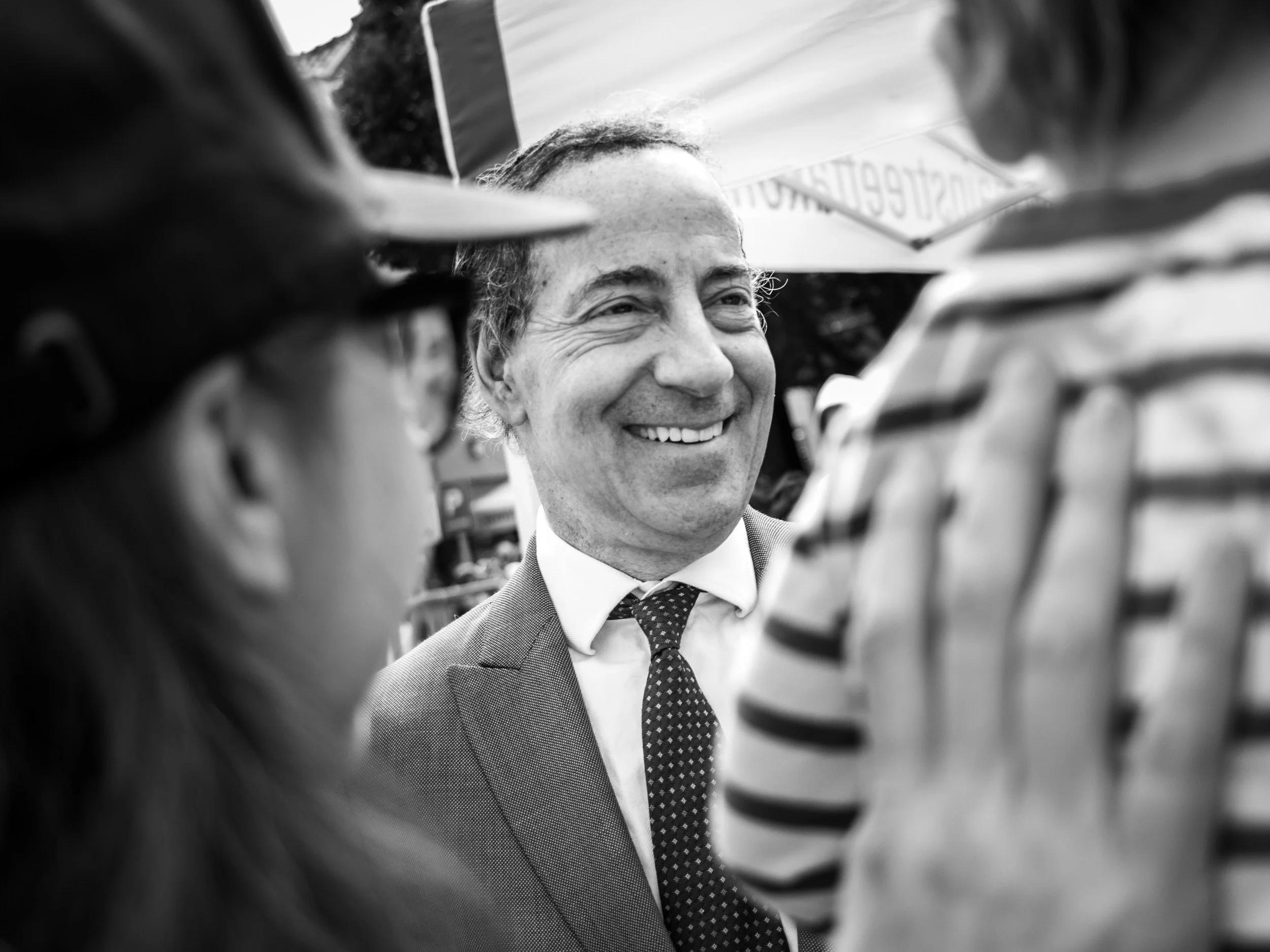 A black and white photo of a smiling man in a suit and tie, surrounded by children wearing helmets, viewed from below.