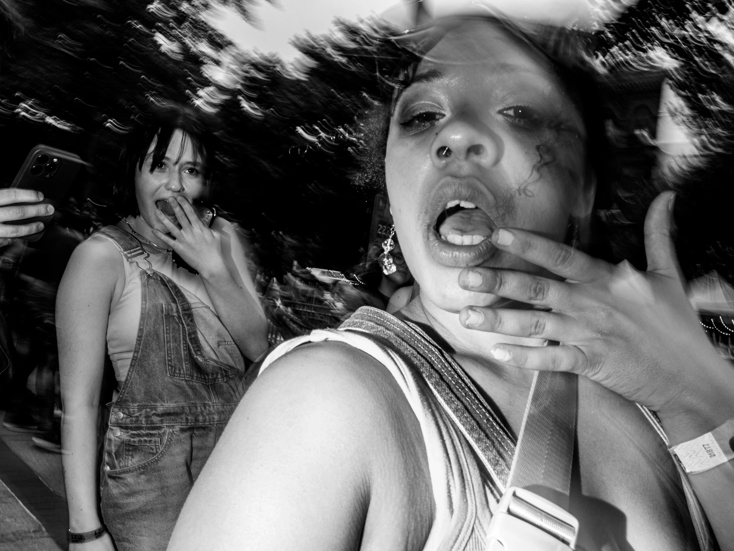 Two women taking a selfie outdoors, one with a big smile and the other making a playful expression, with windblown hair.