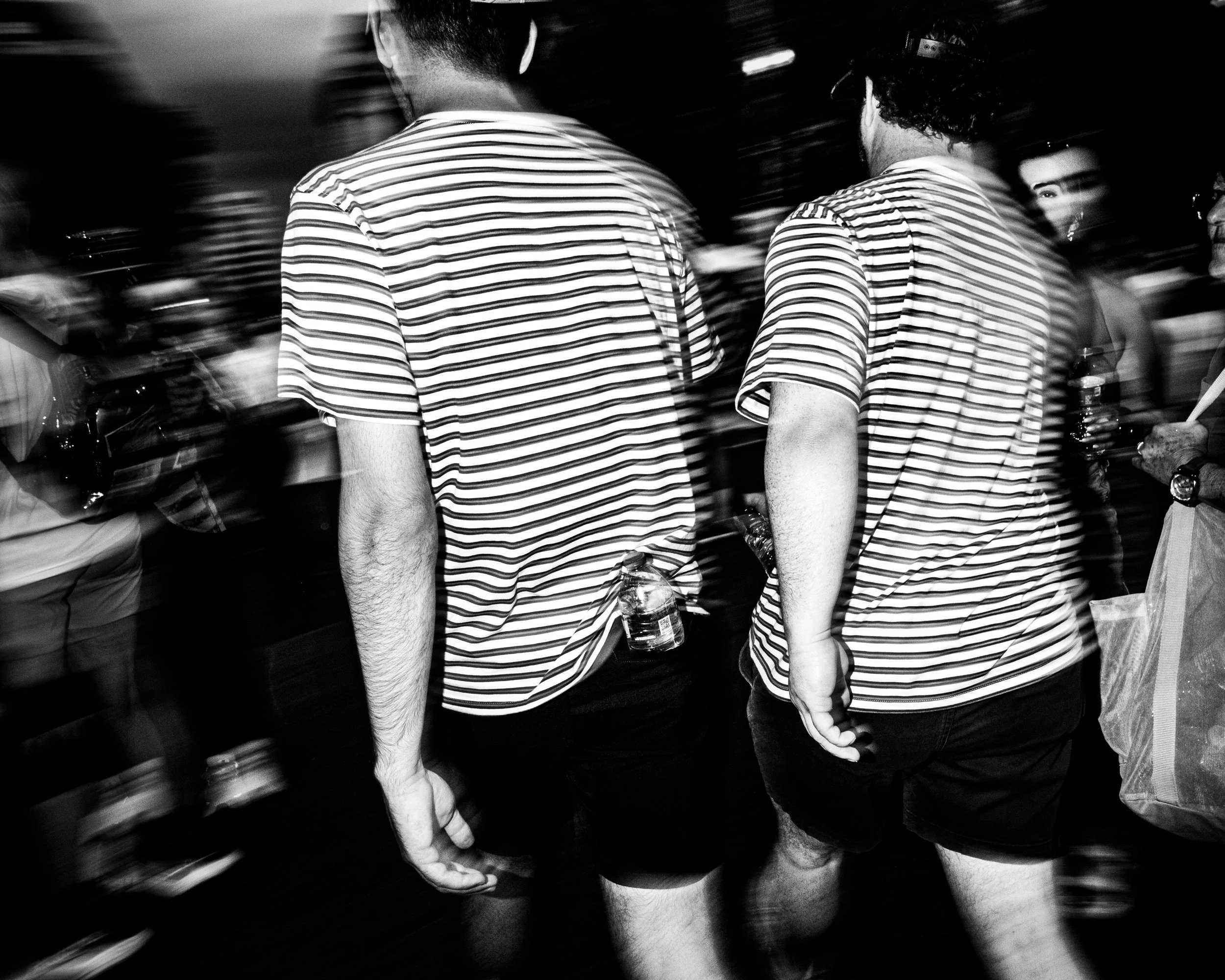 Black and white photo of people from behind, wearing striped shirts, holding water bottles, at what seems to be a social event or gathering.