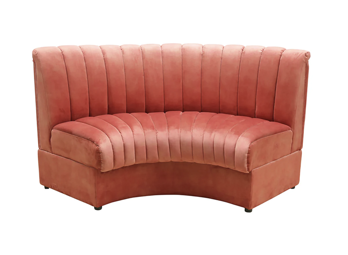 A pink velvet curved corner sofa with vertical channel tufting.