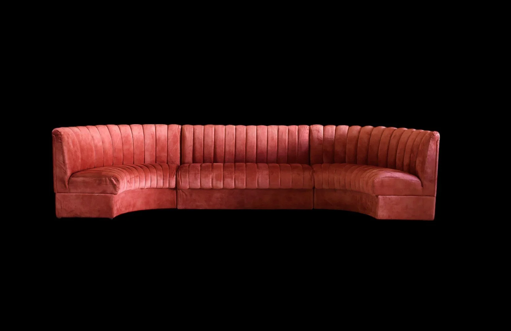 A pink velvet sectional sofa with vertical stitching on a black background.