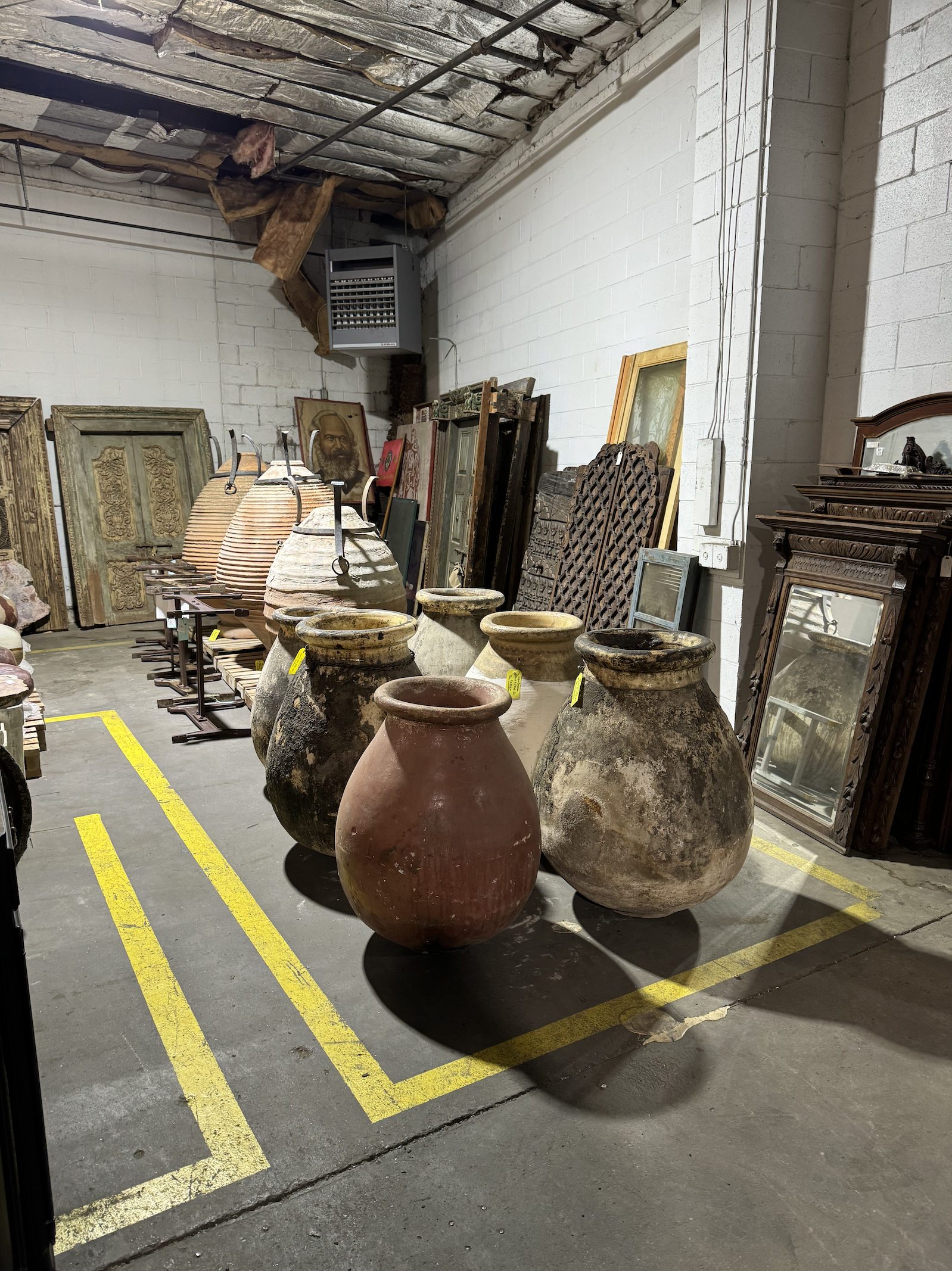 Large antique clay pots and framed artwork in a storage/studio space with white brick walls and a concrete floor.