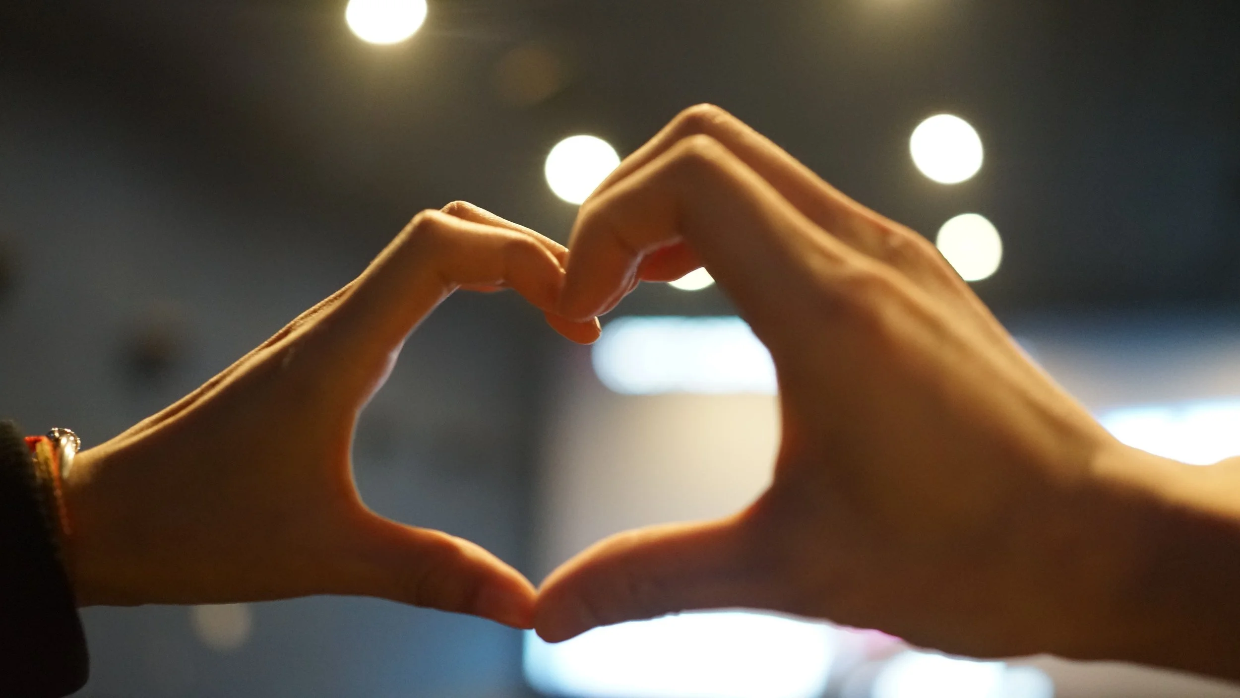 Hands forming a heart shape against a background of circular lights.