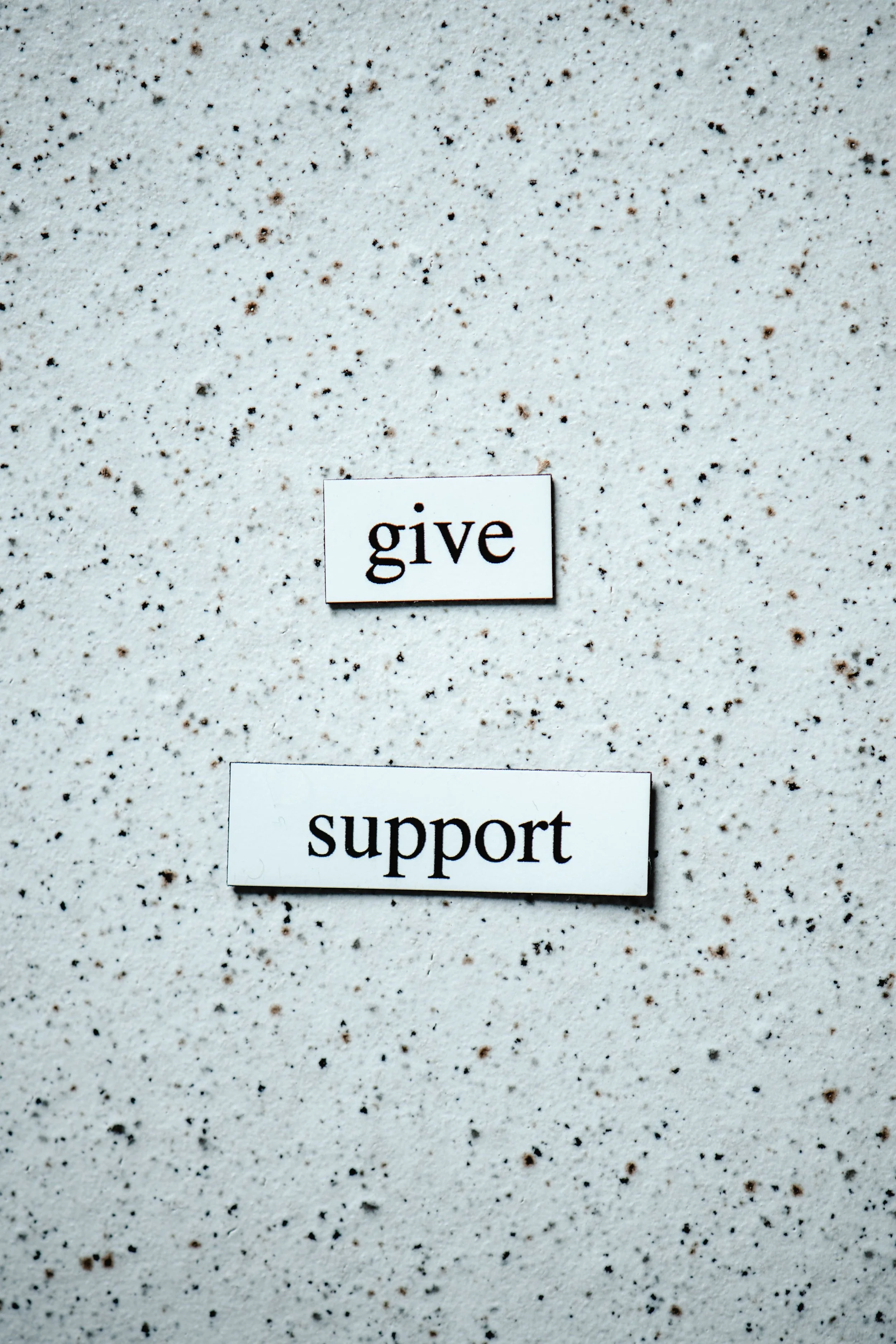 A white wall with small brown and black speckles and two signs reading 'give' and 'support'.