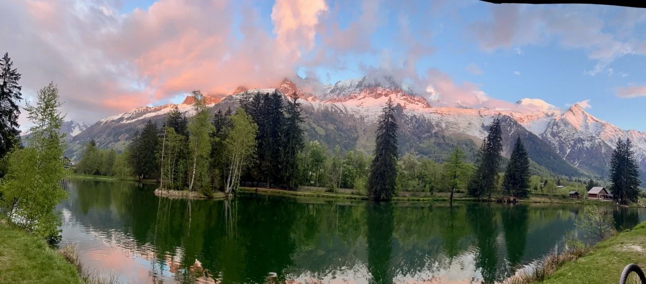 Paysage avec un lac entouré d'arbres et de montagnes enneigées au coucher du soleil.