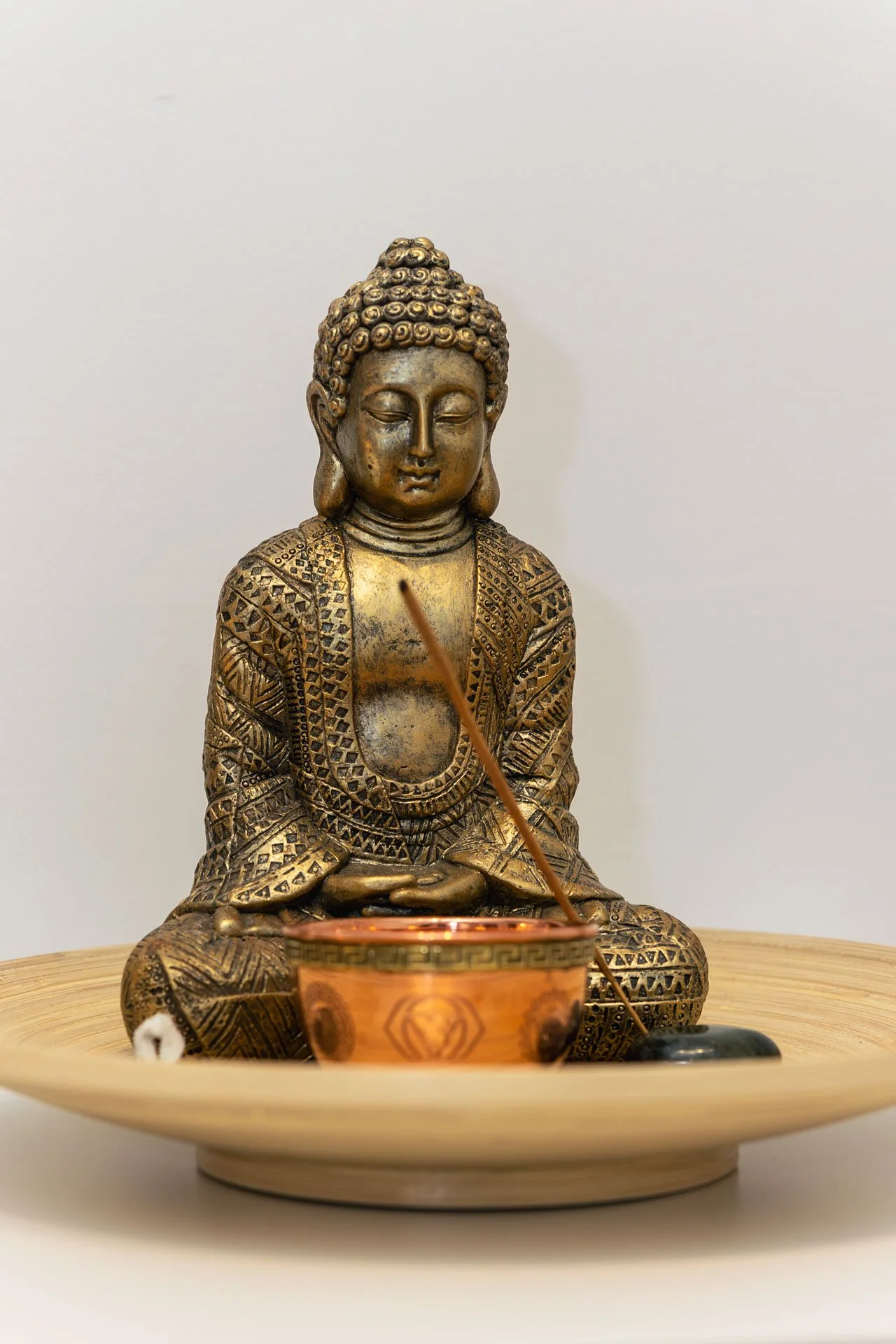 Statue en bronze d'une figure bouddhiste assise en méditation, avec une bougie allumée devant elle, placée sur un plateau en bois.