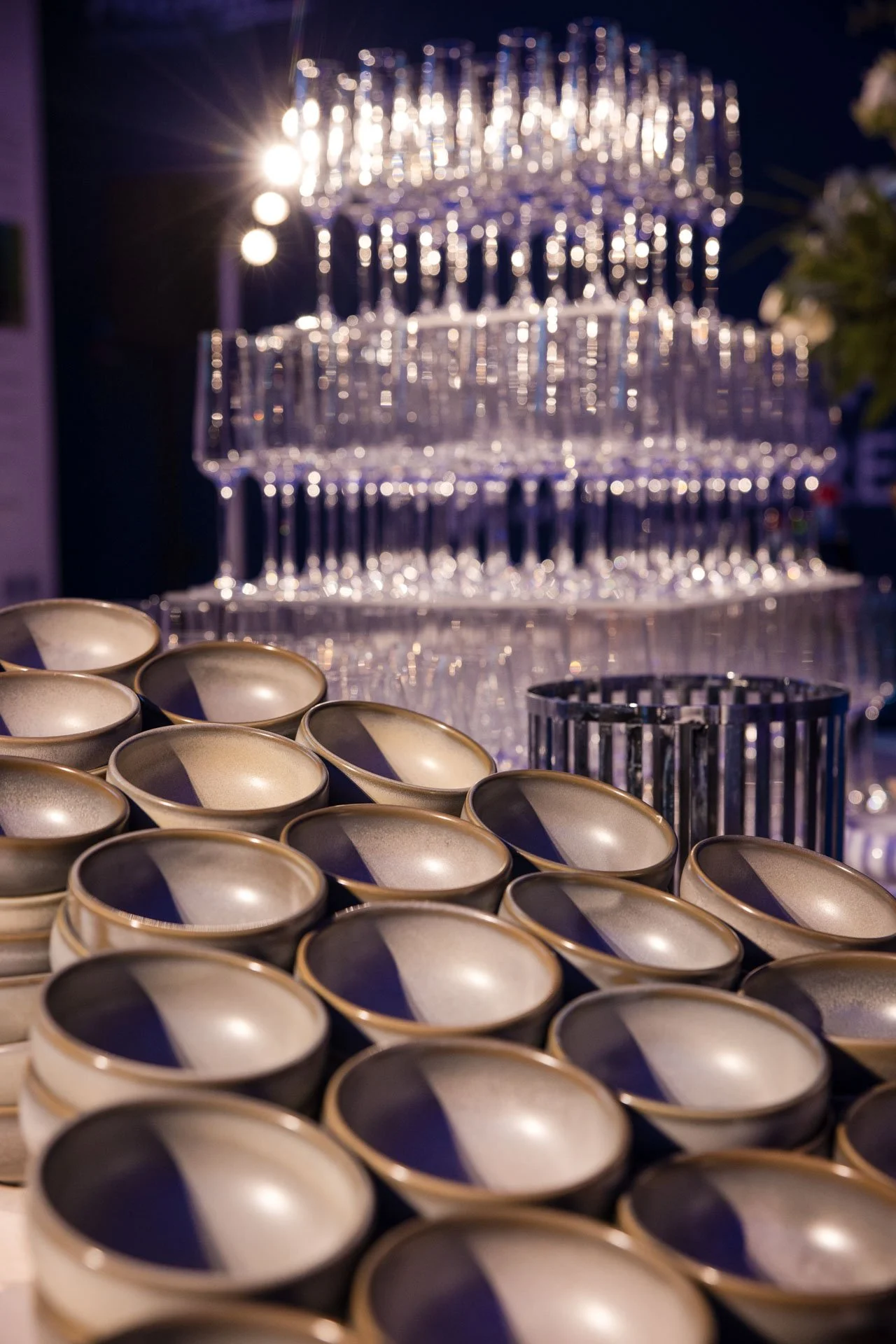 Verres à champagne empilés avec des tasses en porcelaine en avant-plan. Un lustre en cristal brillant en arrière-plan.