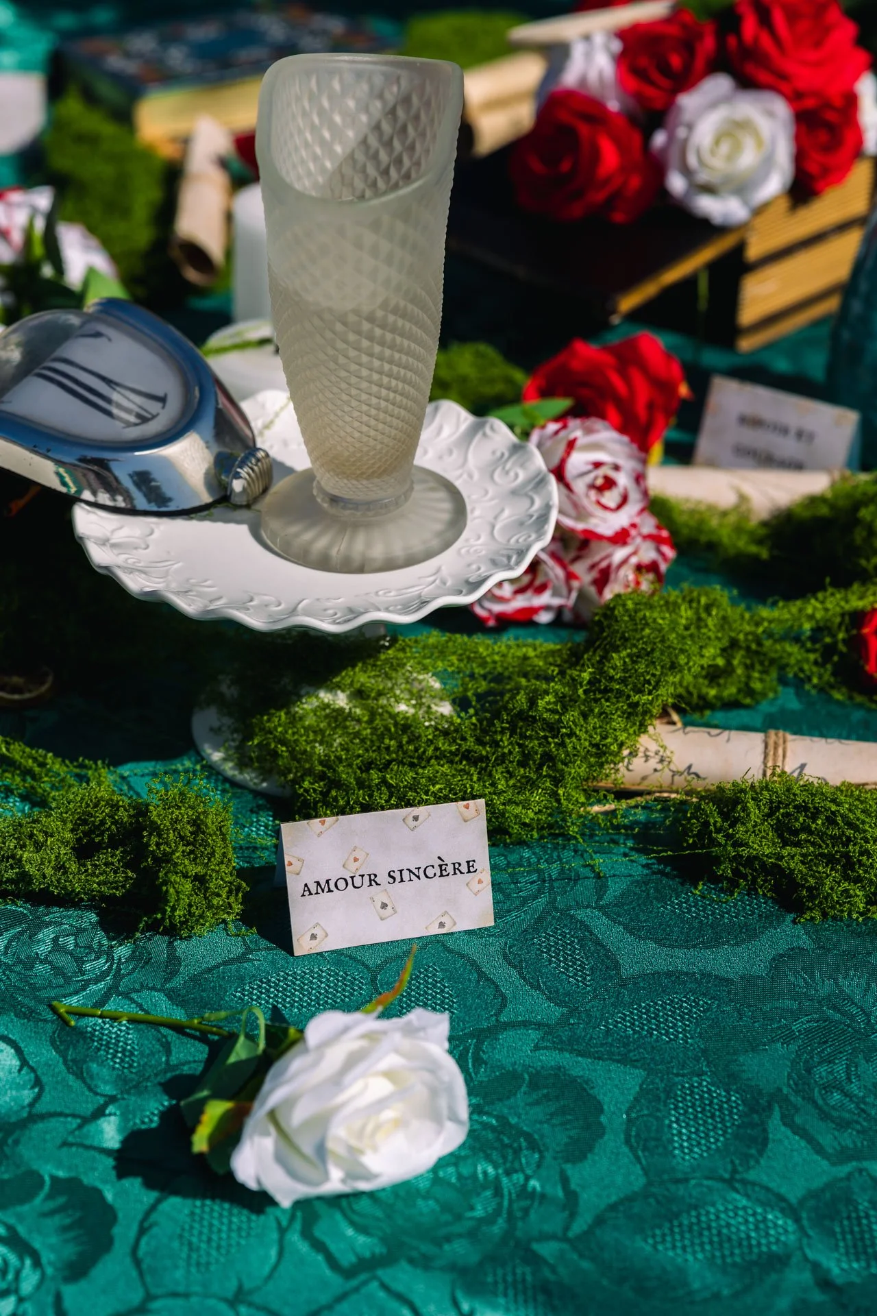 Une table recouverte d'une nappe turquoise, décorée avec des fleurs blanches, un mot 'Amour Sincère' écrit sur une petite carte, et un centre de table avec un verre d'ivoire et des roses rouges et blanches.