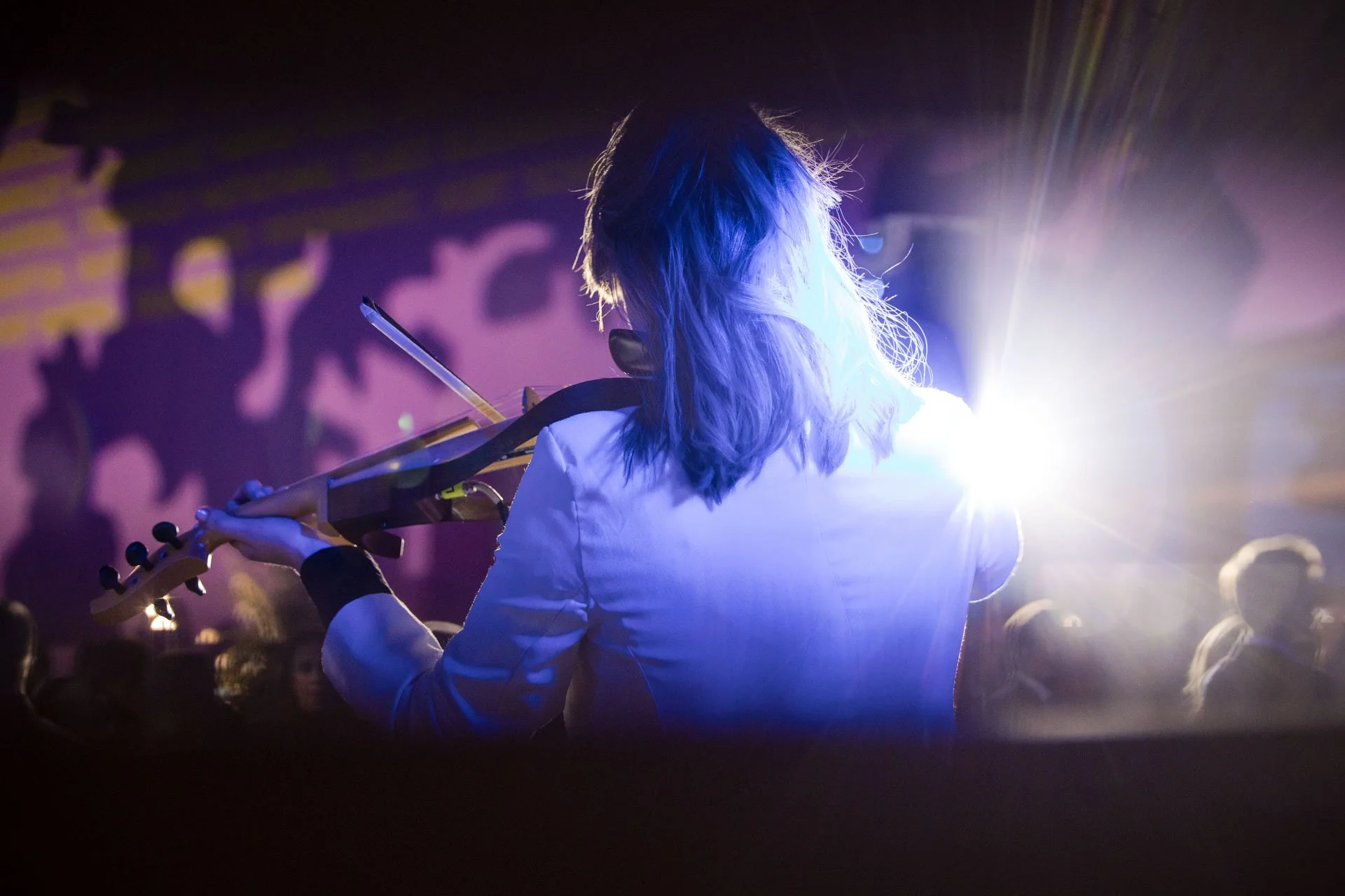 Personne jouant de la guitare électrique sur scène avec un éclairage coloré et une foule en arrière-plan.