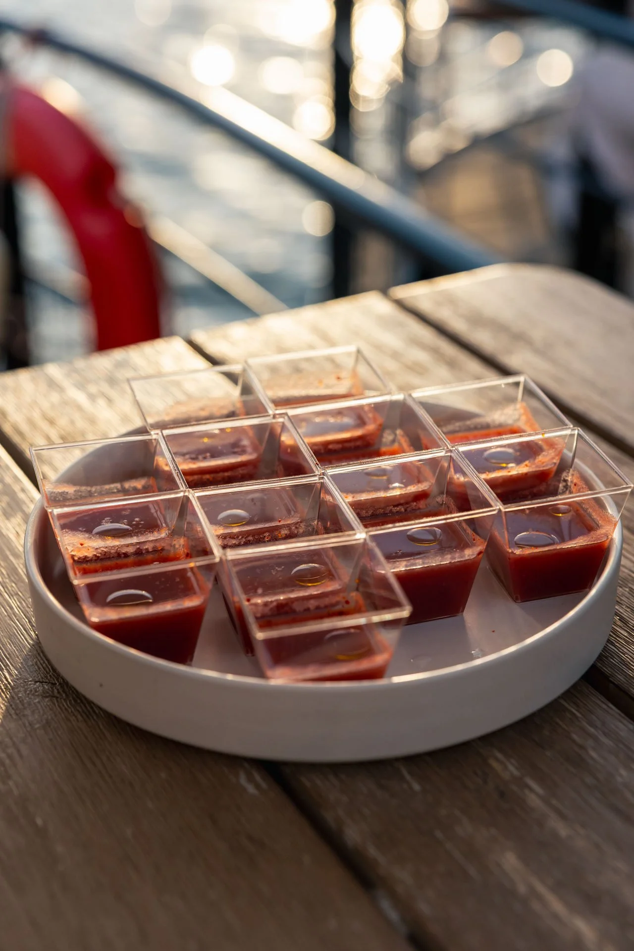 Gobelets en plastique contenant une boisson rouge, disposés dans un plat blanc, placé sur une table en bois lors d'une sortie en extérieur.