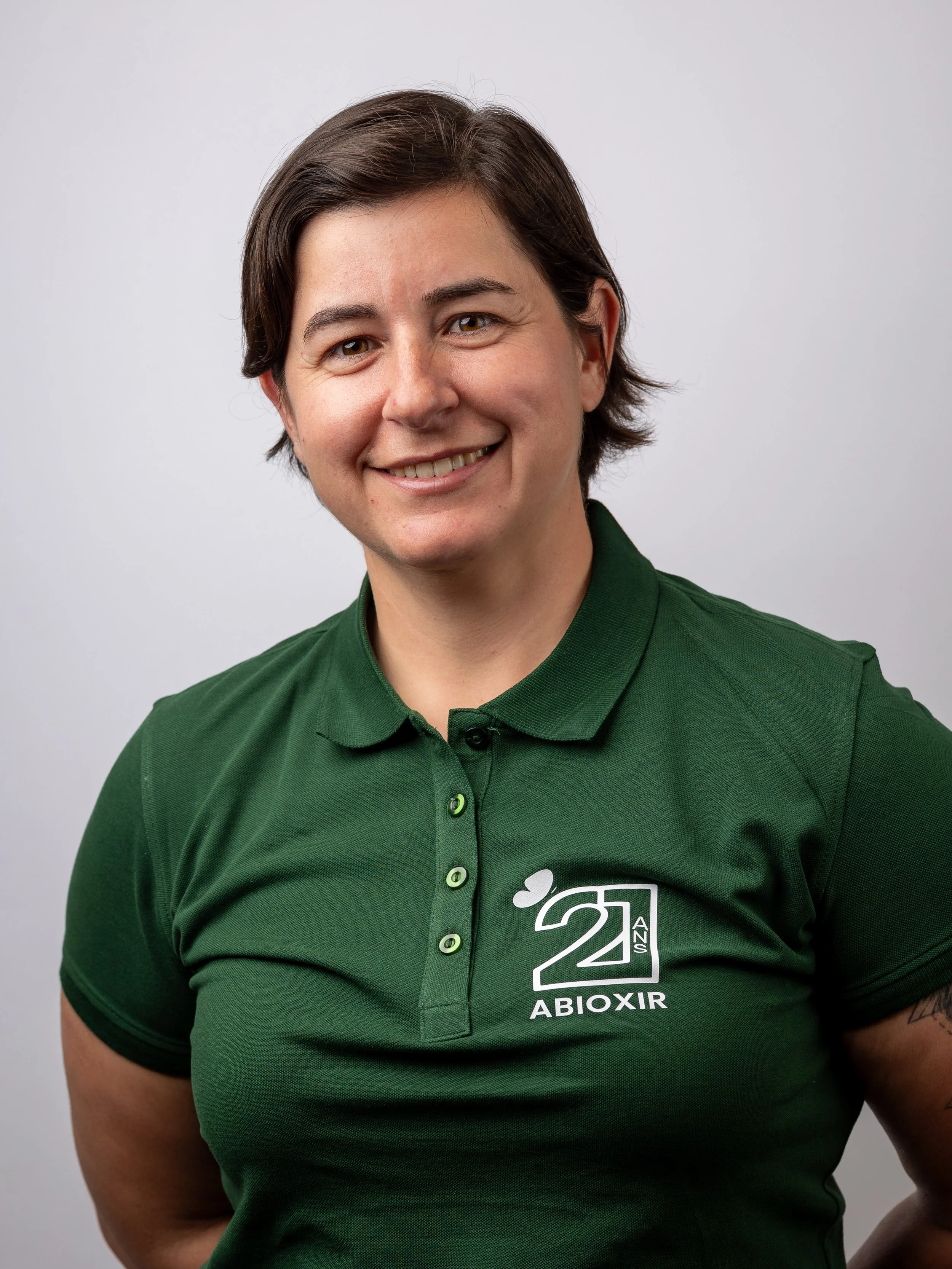 Une femme souriante portant un polo vert avec un logo marquant le 22e anniversaire d'ABIOXIR.