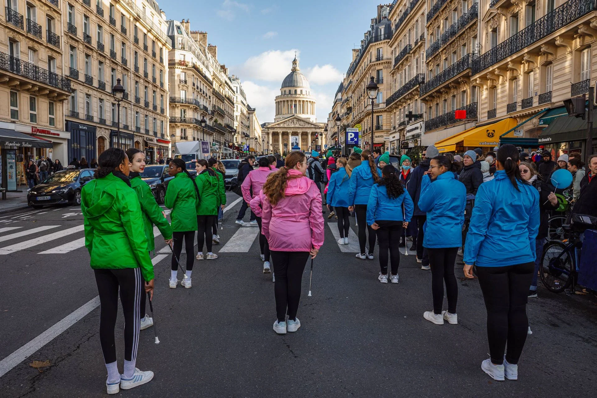Groupe de personnes portant des vestes colorées, marchant dans une rue animée de Paris avec la basilique du Sacré-Cœur en arrière-plan.
