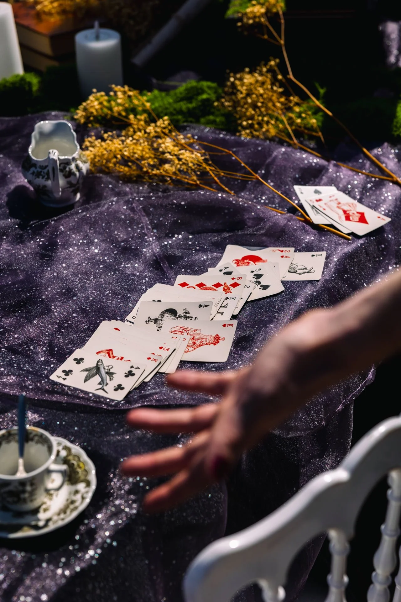 Un jeu de cartes étalé sur une surface noire avec des fleurs jaunes, une tasse à thé, et des bougies dans le fond.