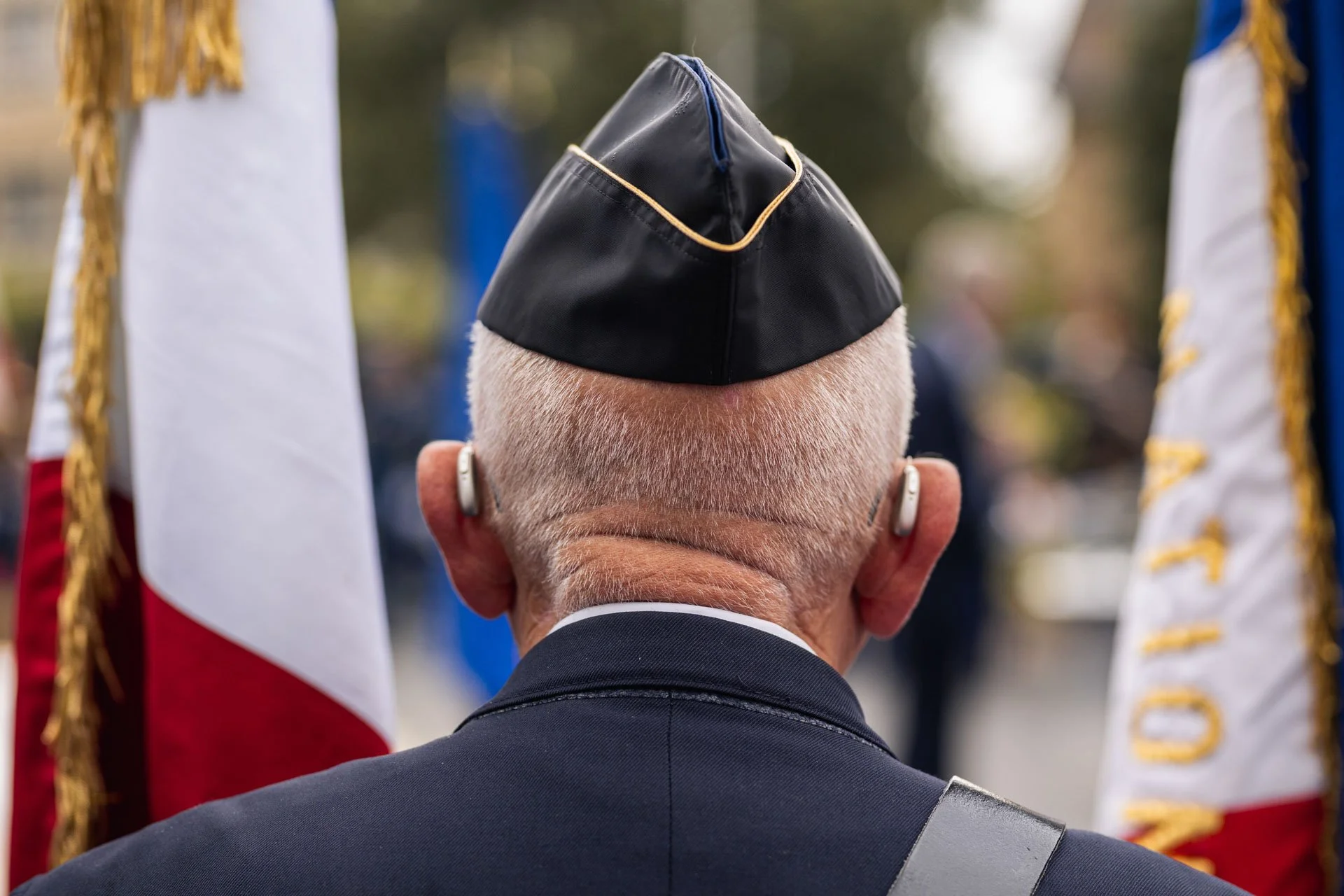 Un homme âgé à la tête chauve portant une uniforme militaire regarde un drapeau lors d'une cérémonie officielle.