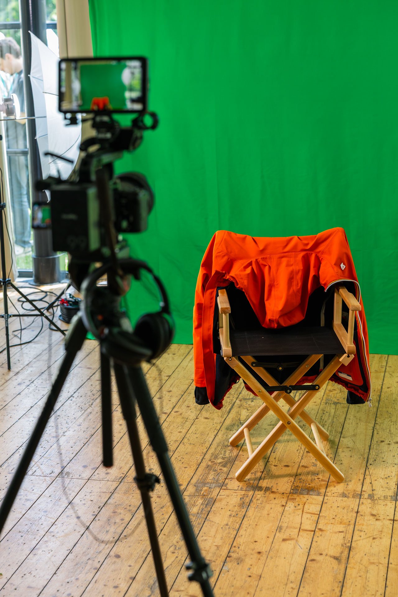 Un fauteuil pliant en bois avec une veste de couleur orange dessus, devant un fond vert d'écran vert, dans un studio de tournage.