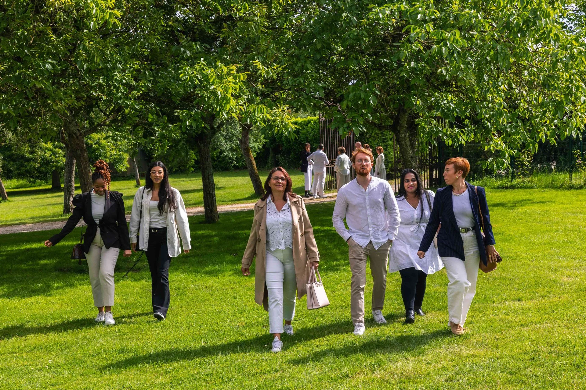 Groupe de personnes marchant dans un parc verdoyant entouré d'arbres, en tenue décontractée et élégante.