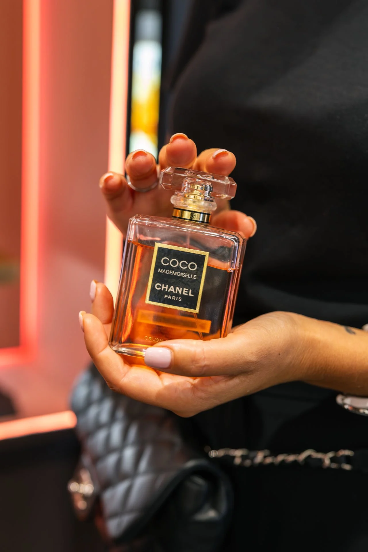 Une personne tient un flacon de parfum Chanel Coco Mademoiselle avec un fond flou.