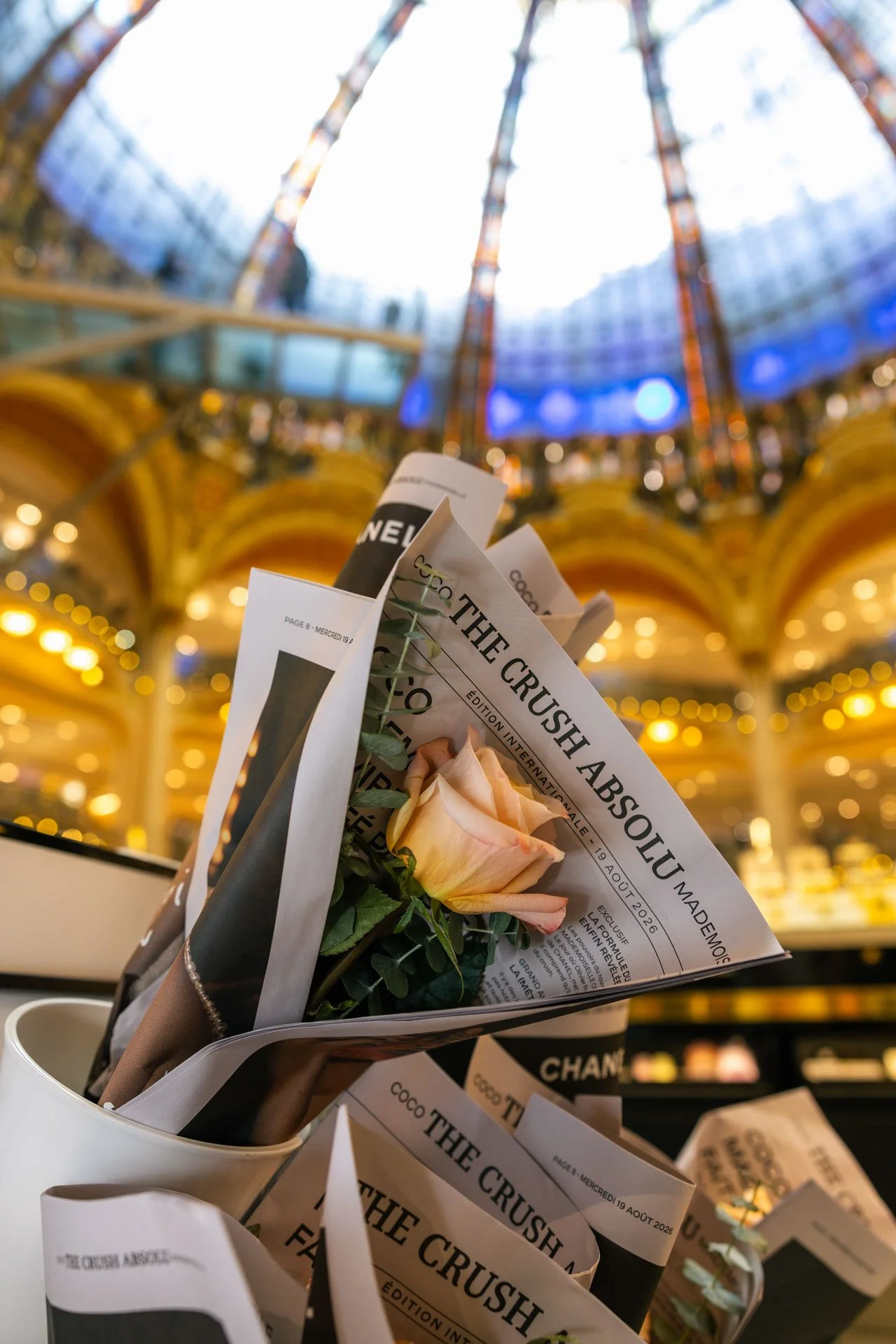 Fleurs roses dans un journal avec une architecture en verre et métal au plafond, couleurs chaudes et lumières dans un intérieur élégant.