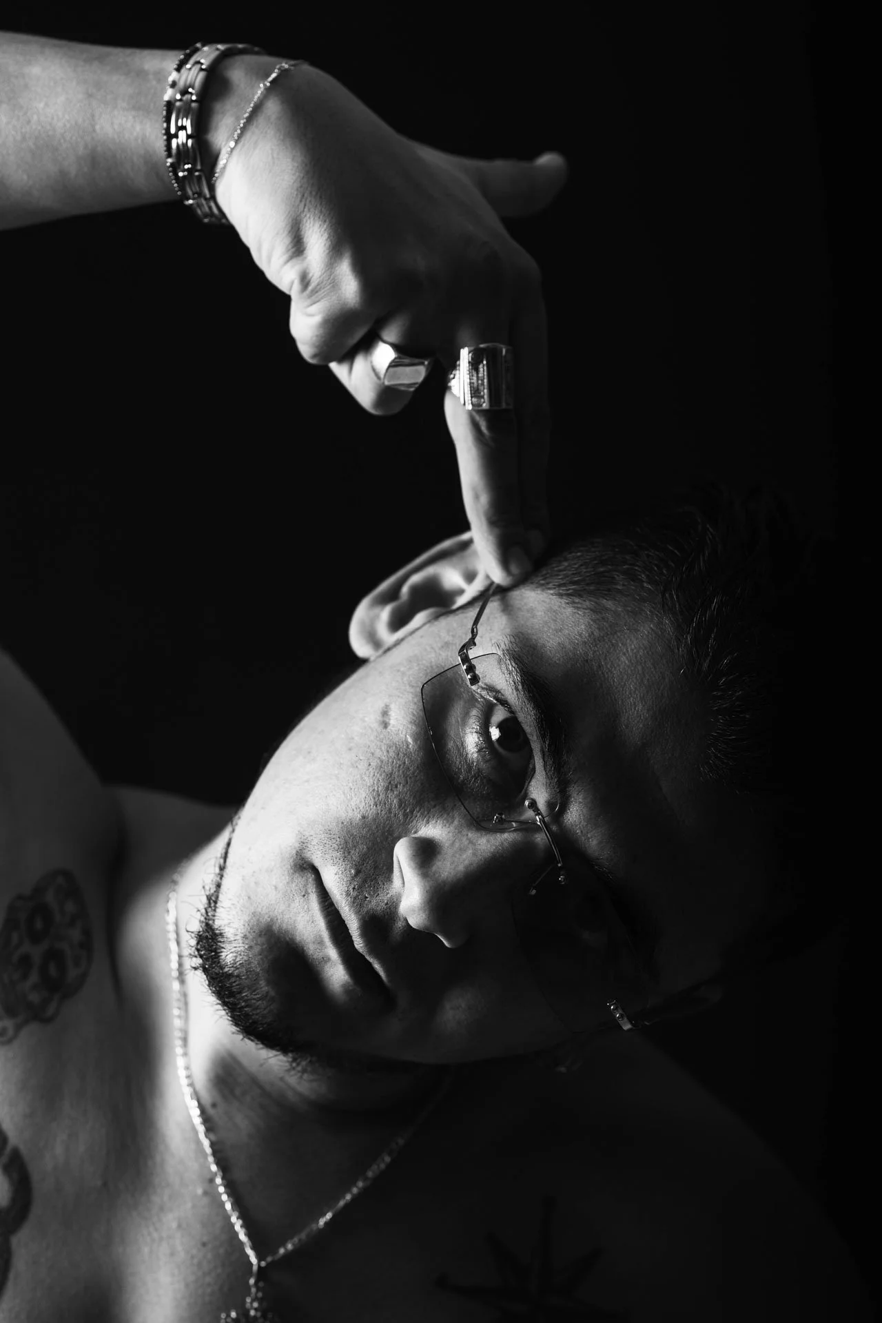 Un jeune homme avec des lunettes et une barbe, allongé sur le dos, recevant une injection ou une procédure médicale au visage, en noir et blanc.