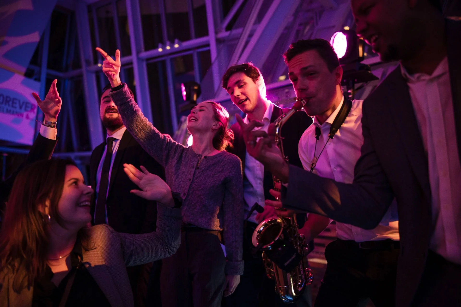 Groupe de jeunes adultes jouant de la musique et dansant lors d'une fête ou d'un événement en intérieur, avec des lumières colorées et une ambiance festive.