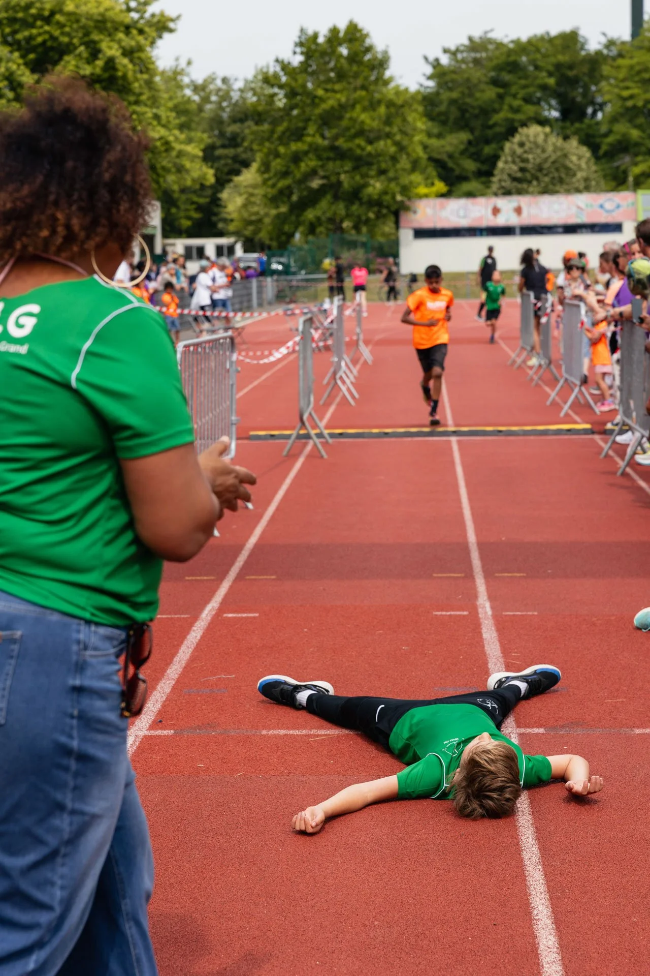 Un enfant allongé par terre après une course, à côté d'une ligne de finish, avec d'autres enfants et spectateurs en arrière-plan, lors d'une compétition sportive