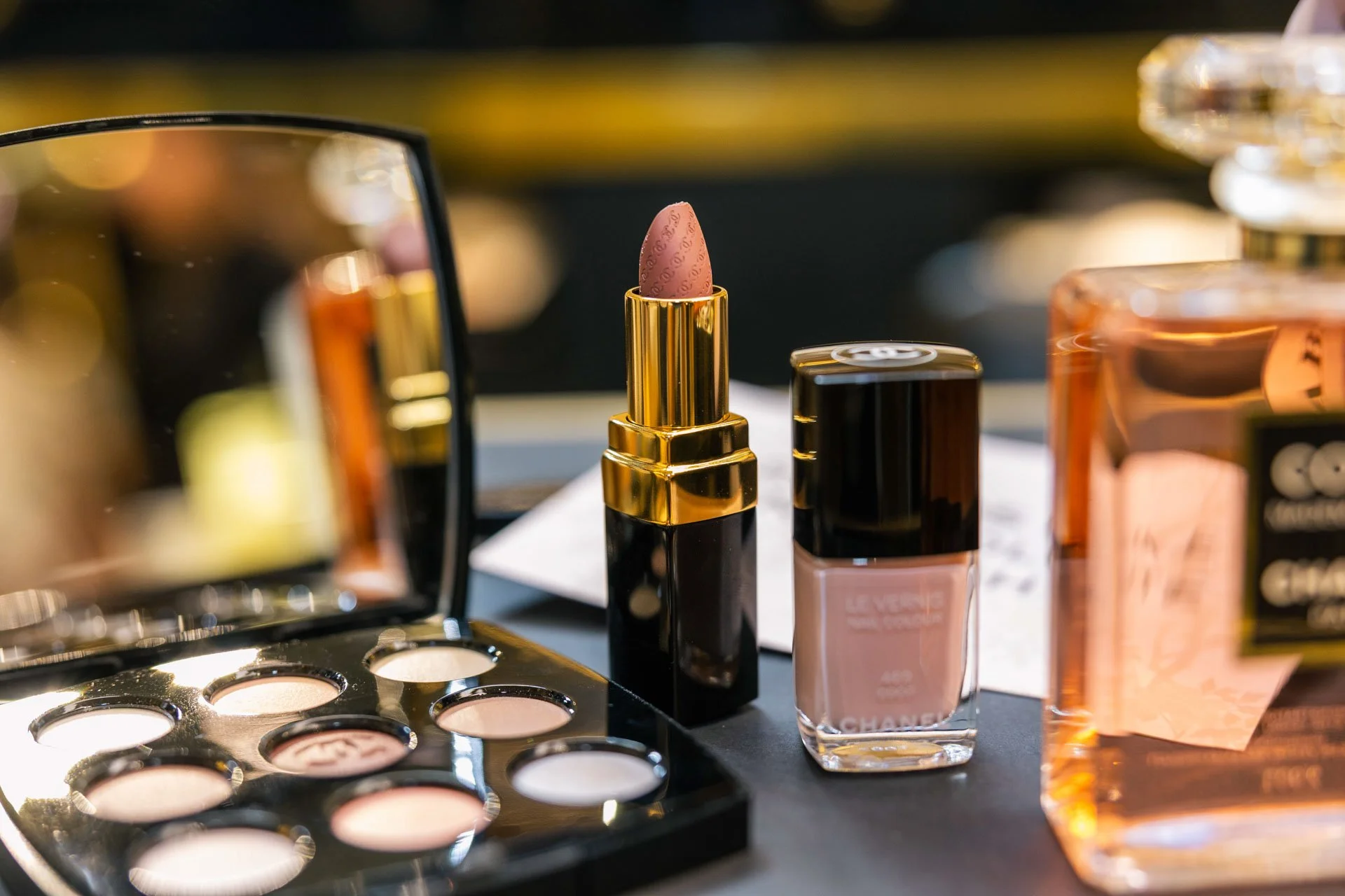 Vernis à ongles rose, rouge à lèvres et autres produits cosmétiques sur un meuble.