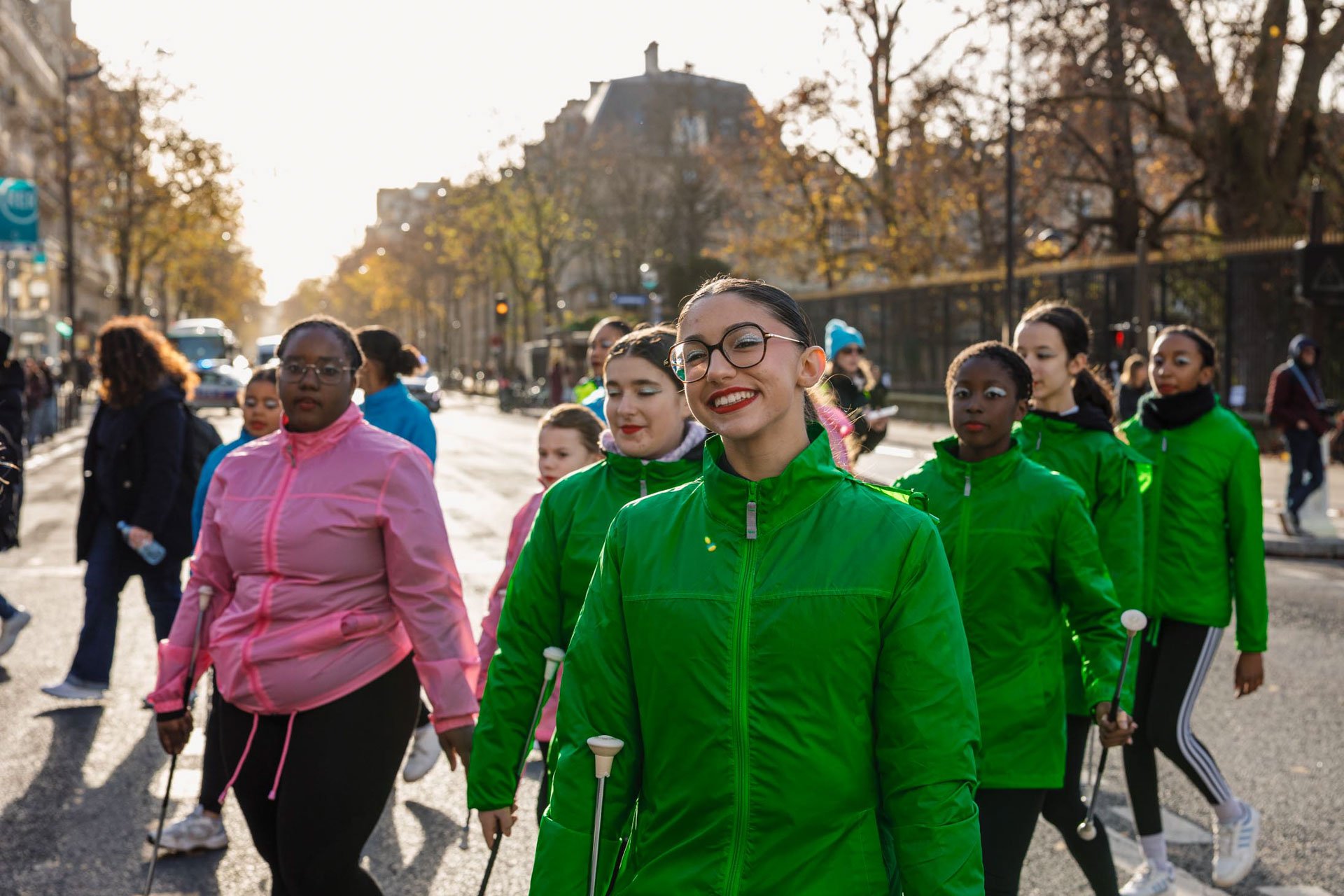 Groupe de femmes marchant dans la rue par une journée ensoleillée, portant des tenues colorées, arbres en automne en arrière-plan.