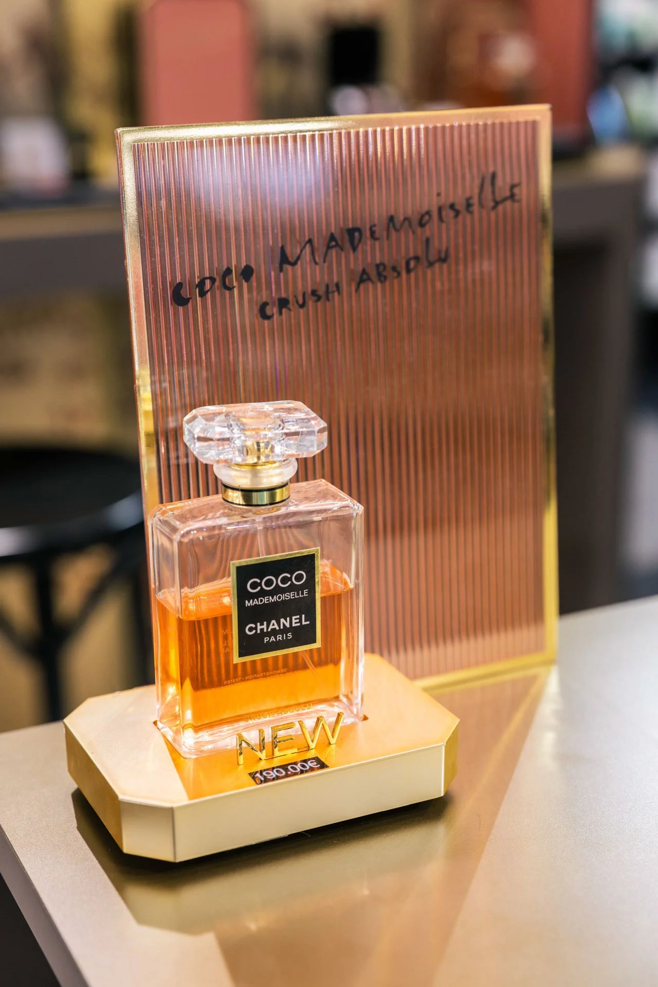Une bouteille de parfum Chanel Coco Mademoiselle avec un fond rose à lignes verticales.