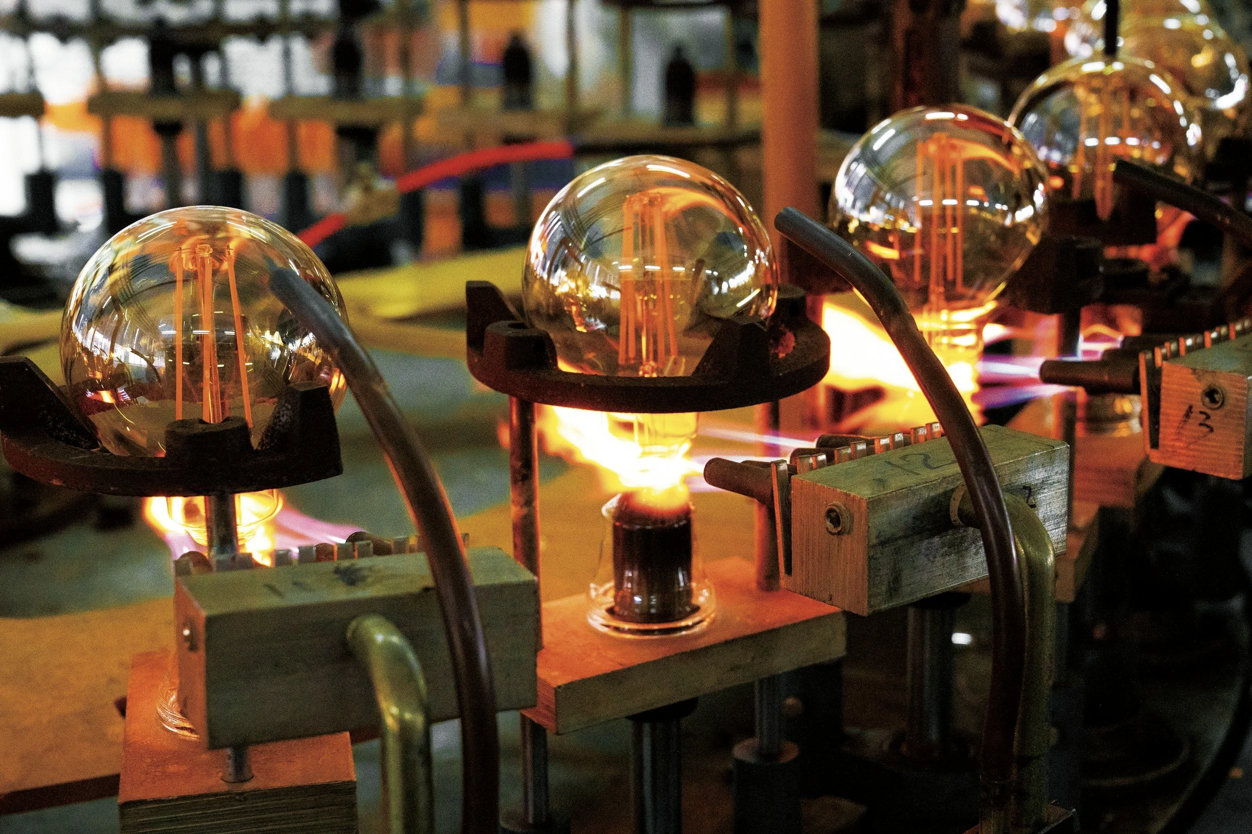 Close-up of glowing light bulbs with filament visible, connected to a circuit with wooden and metal components, in a dark setting.