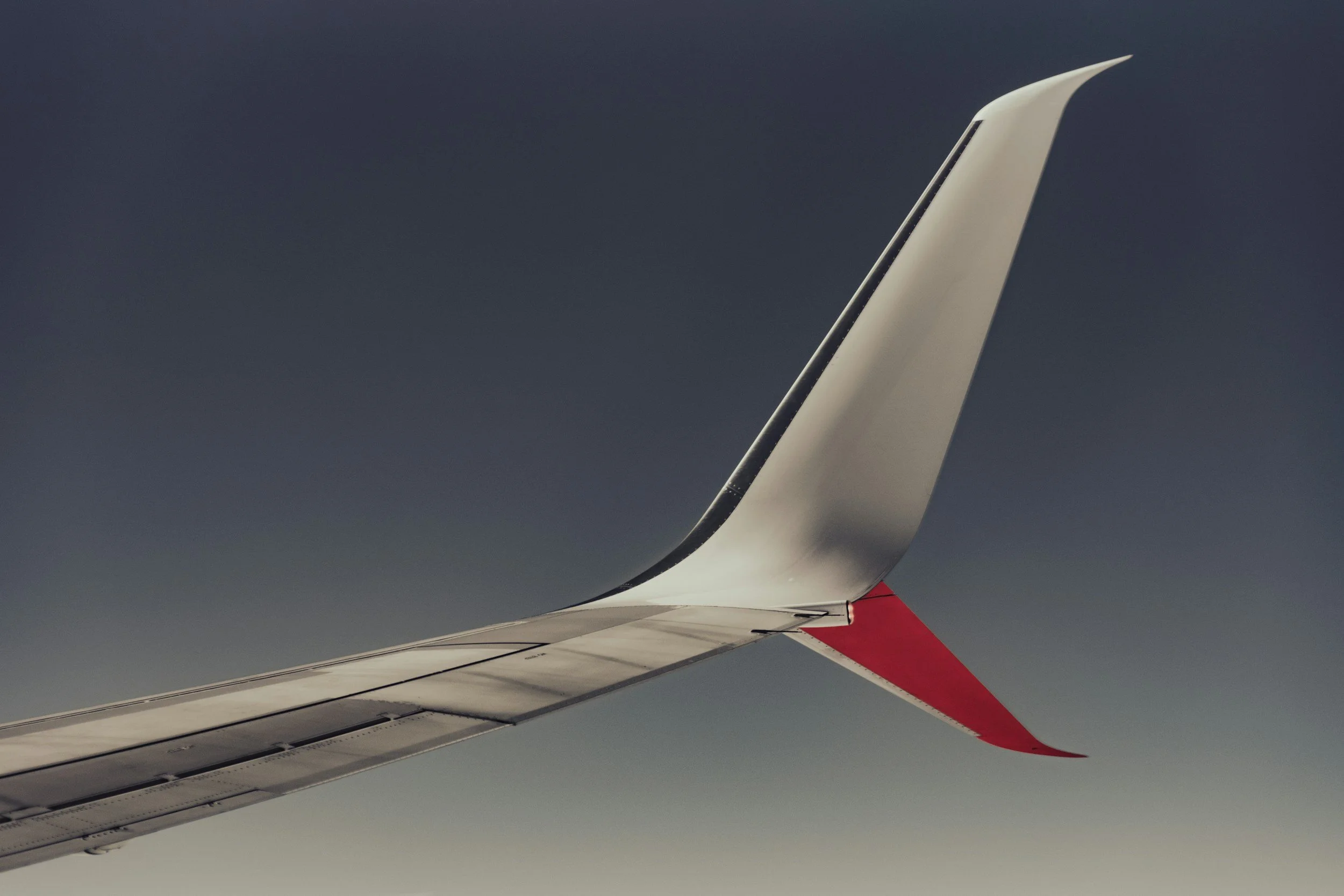 View of airplane wing with red wingtip against a dark gray sky.