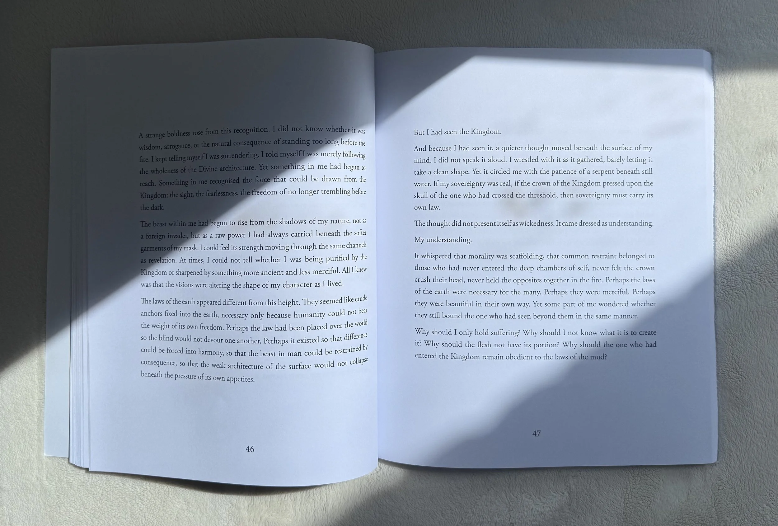 Open book on a light-colored surface with sunlight casting a shadow across the pages, numbered 46 and 47, displaying text.