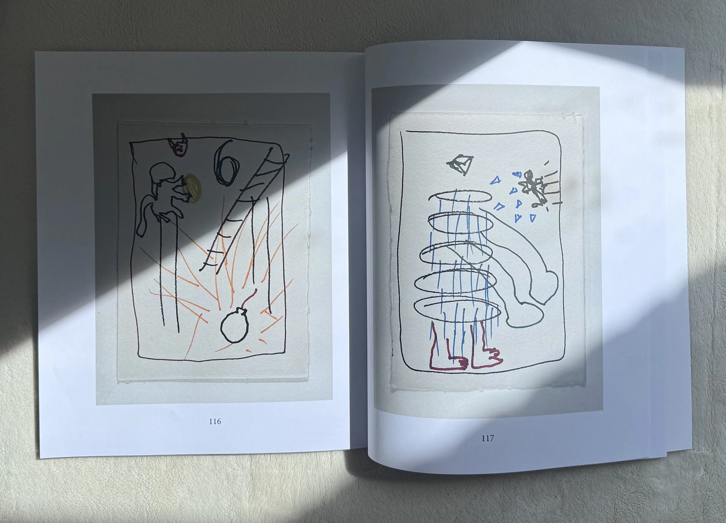 Open notebook with two pages of abstract line drawings, one on the left and one on the right, with sunlight rays casting across the pages.