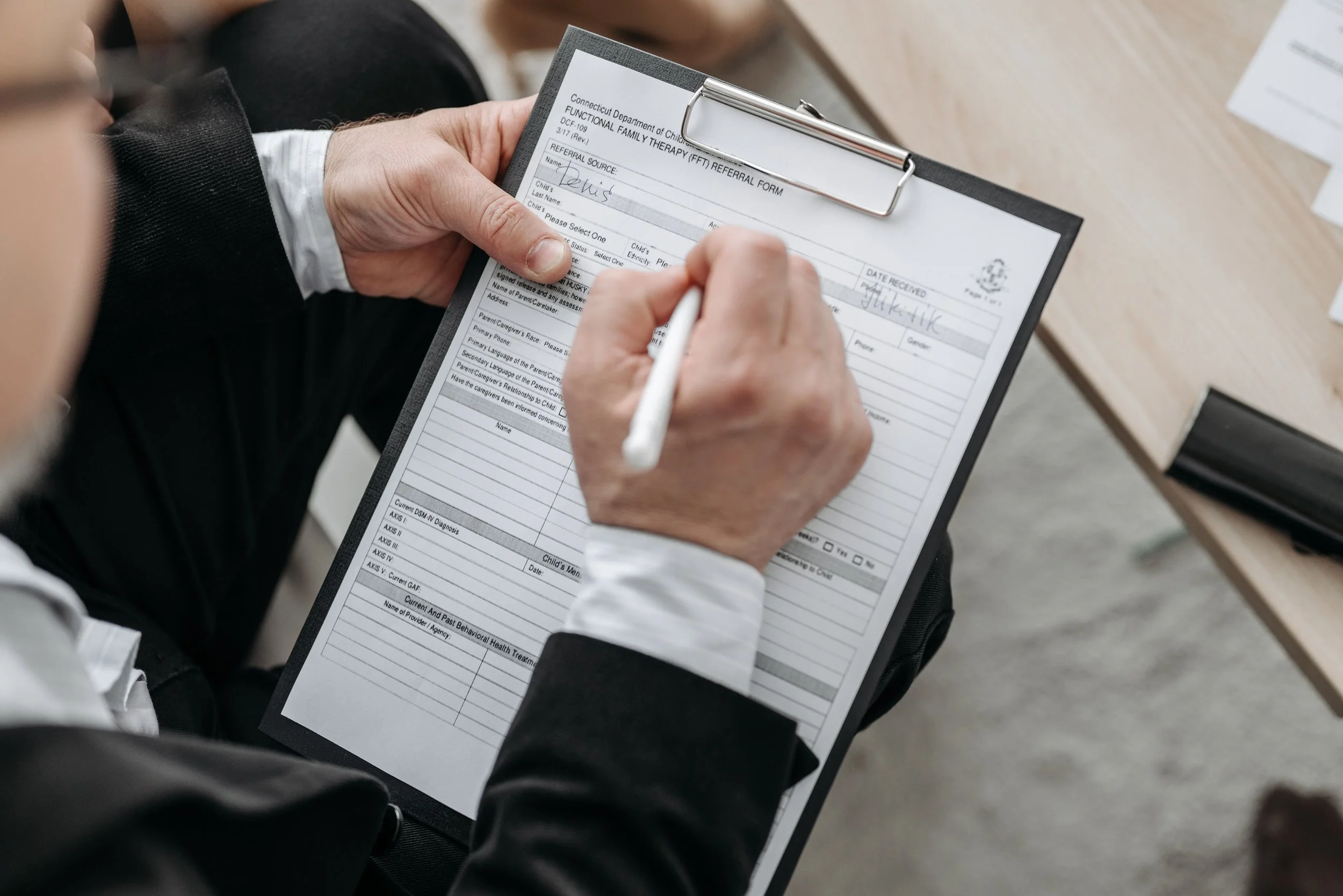 Person filling out a healthcare referral form on a clipboard, seated at a wooden table.