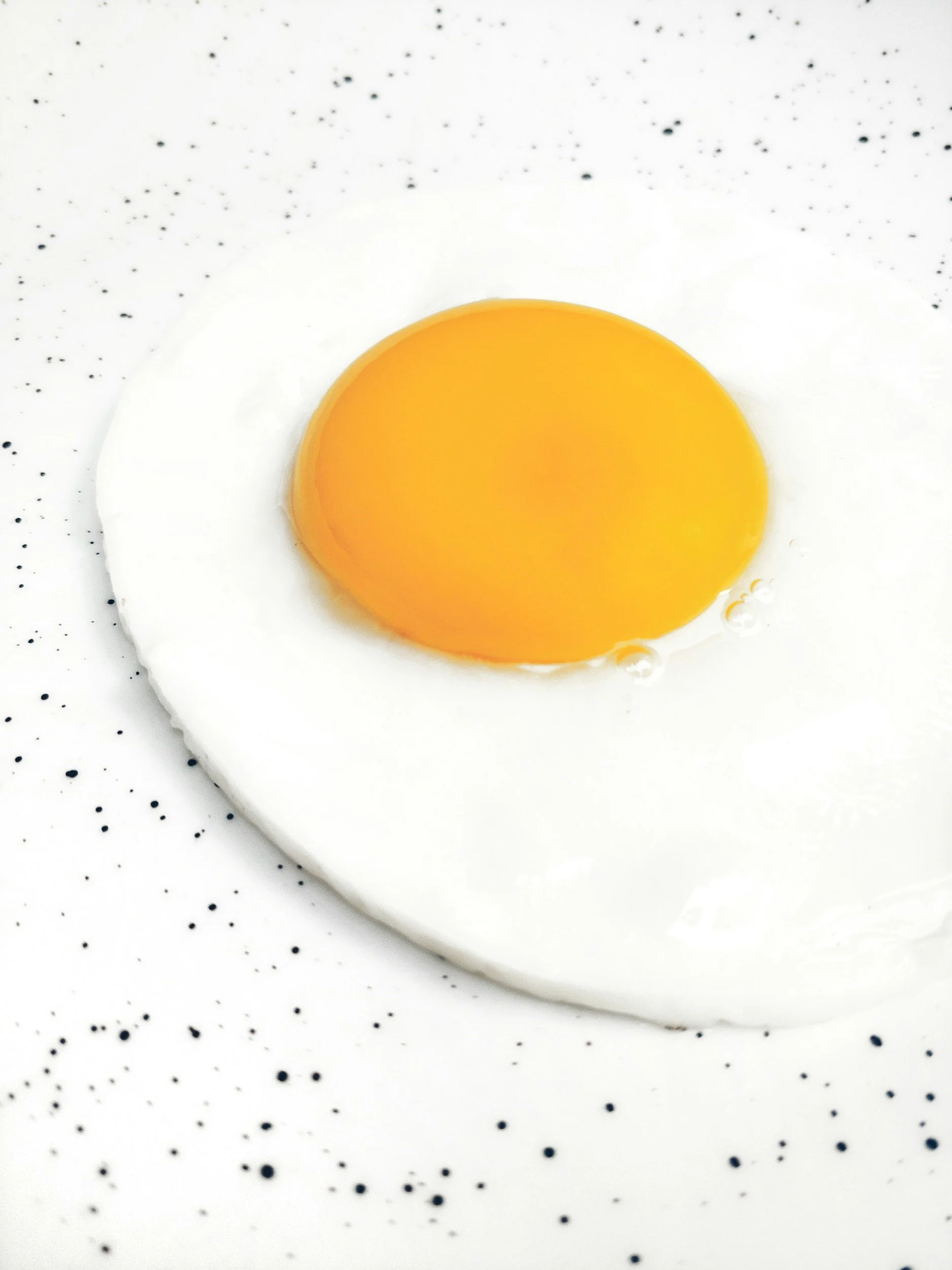 Close-up of a fried egg on a speckled white plate.