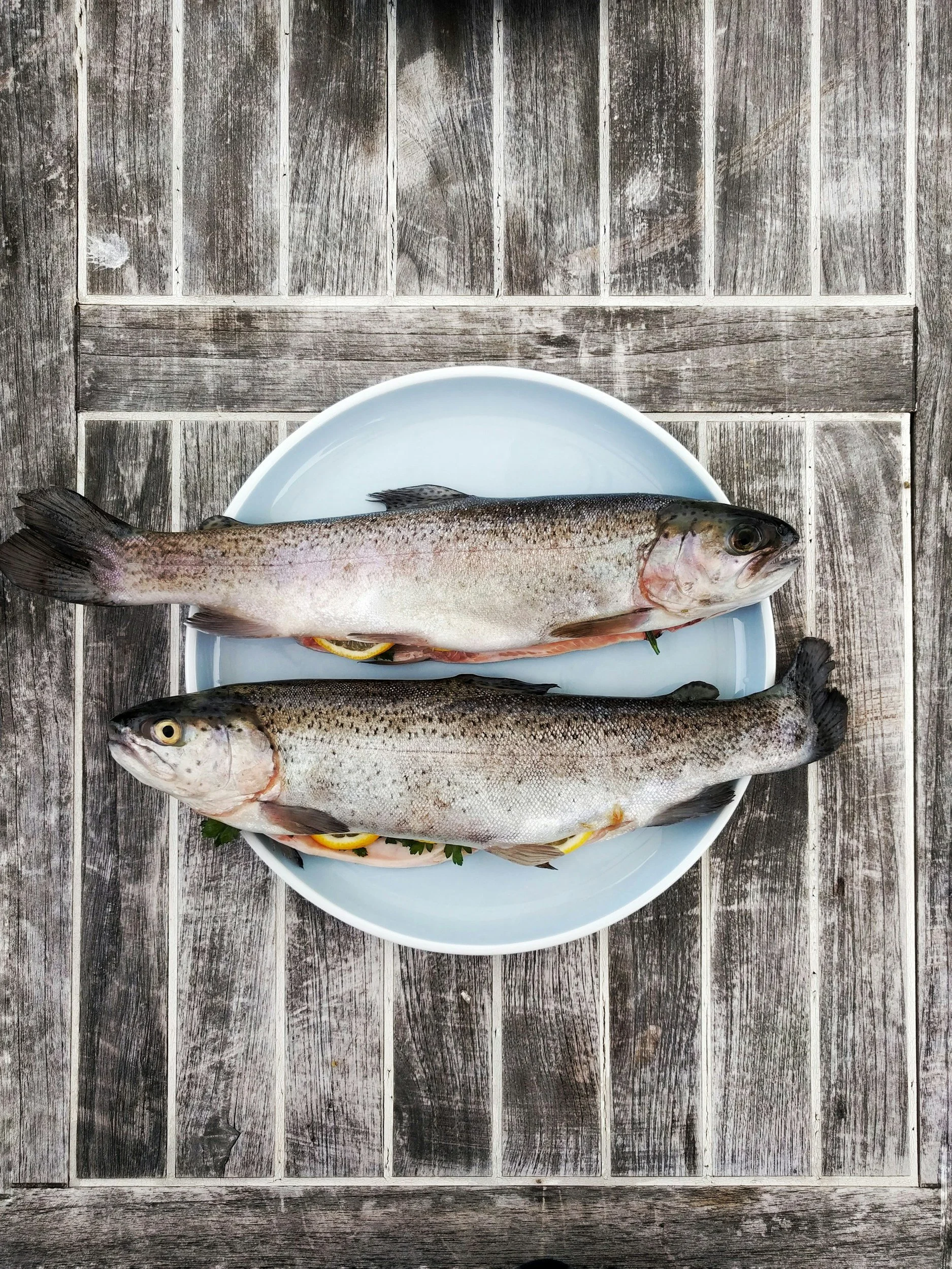 Two whole fish on a white plate set on a weathered wooden surface.