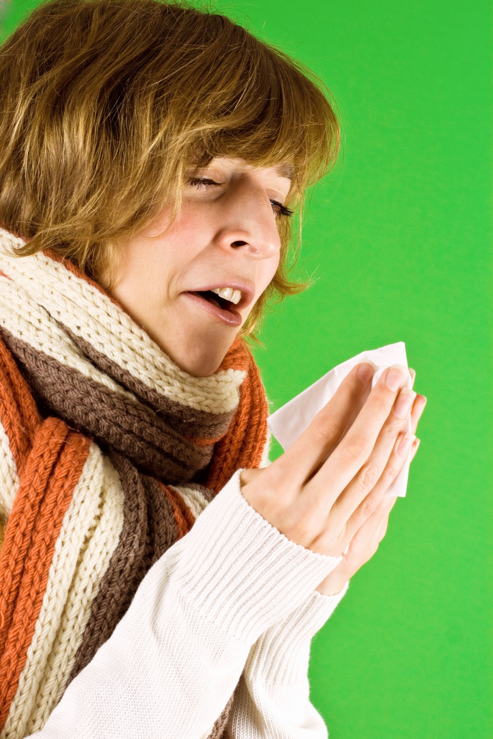 Woman with short brown hair and a knitted scarf, praying with her eyes closed, against a green background.