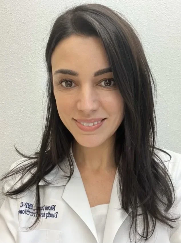 A woman with long dark hair smiling, wearing a white medical uniform.