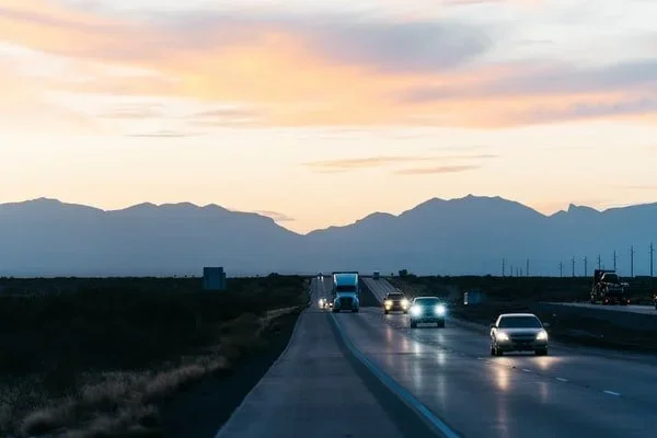 Cars driving on a highway at sunset with mountains in the background