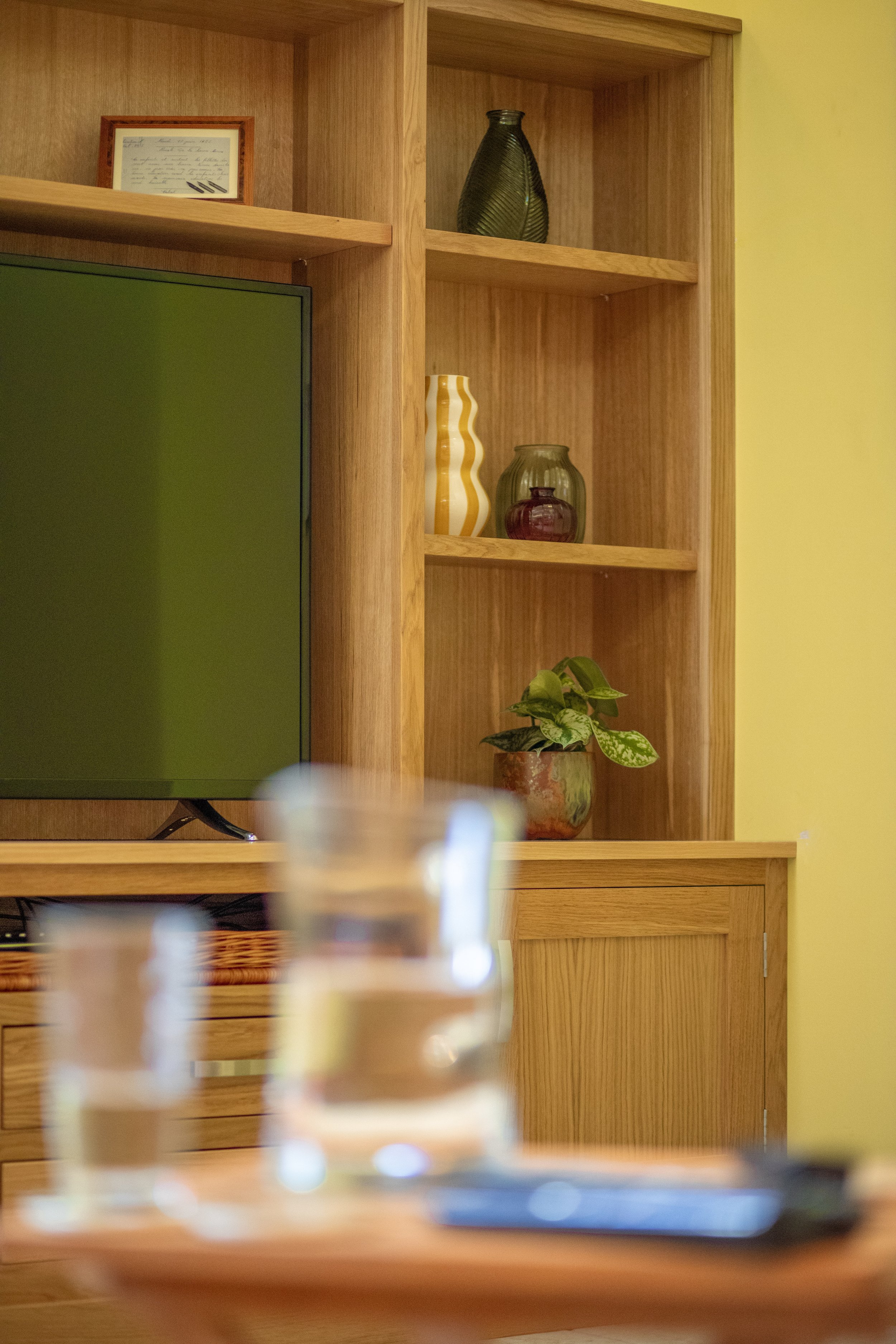 A wooden entertainment center with shelves, holding decorative vases and a framed certificate or photo, with a TV screen partly visible on the left.
