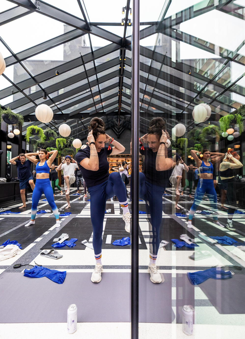 Group fitness class with women in athletic wear, mirrored wall, and glass ceiling, participating in a workout session.