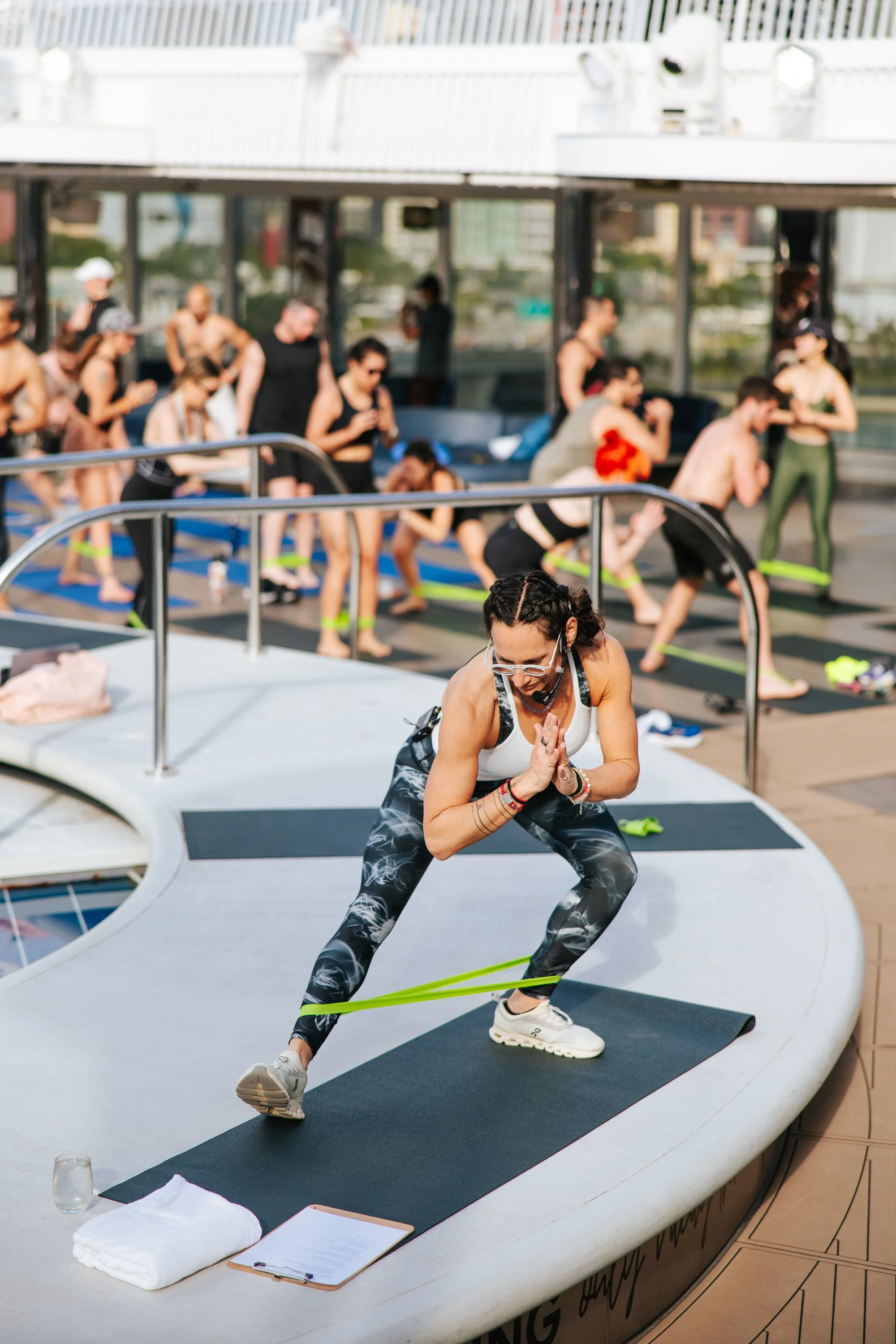 A woman doing yoga on a mat on a boat deck with a group of people in the background practicing yoga or stretching.
