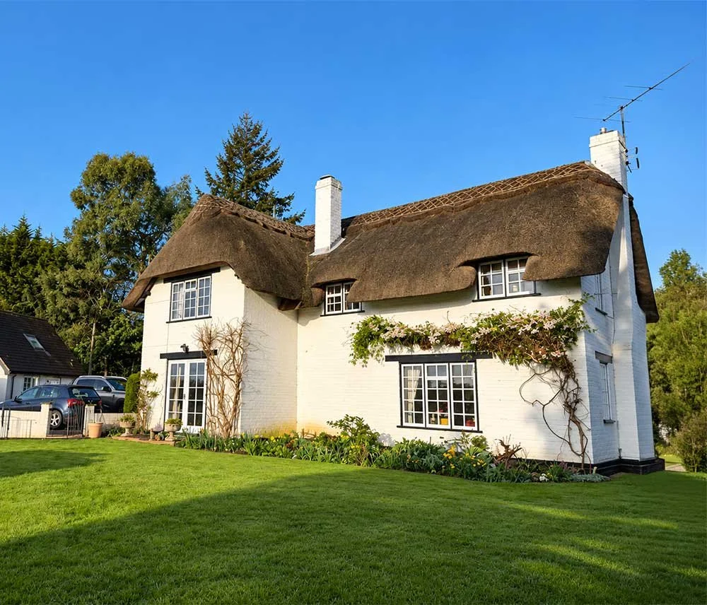 Traditional white cottage with a thatched roof and landscaped front garden.